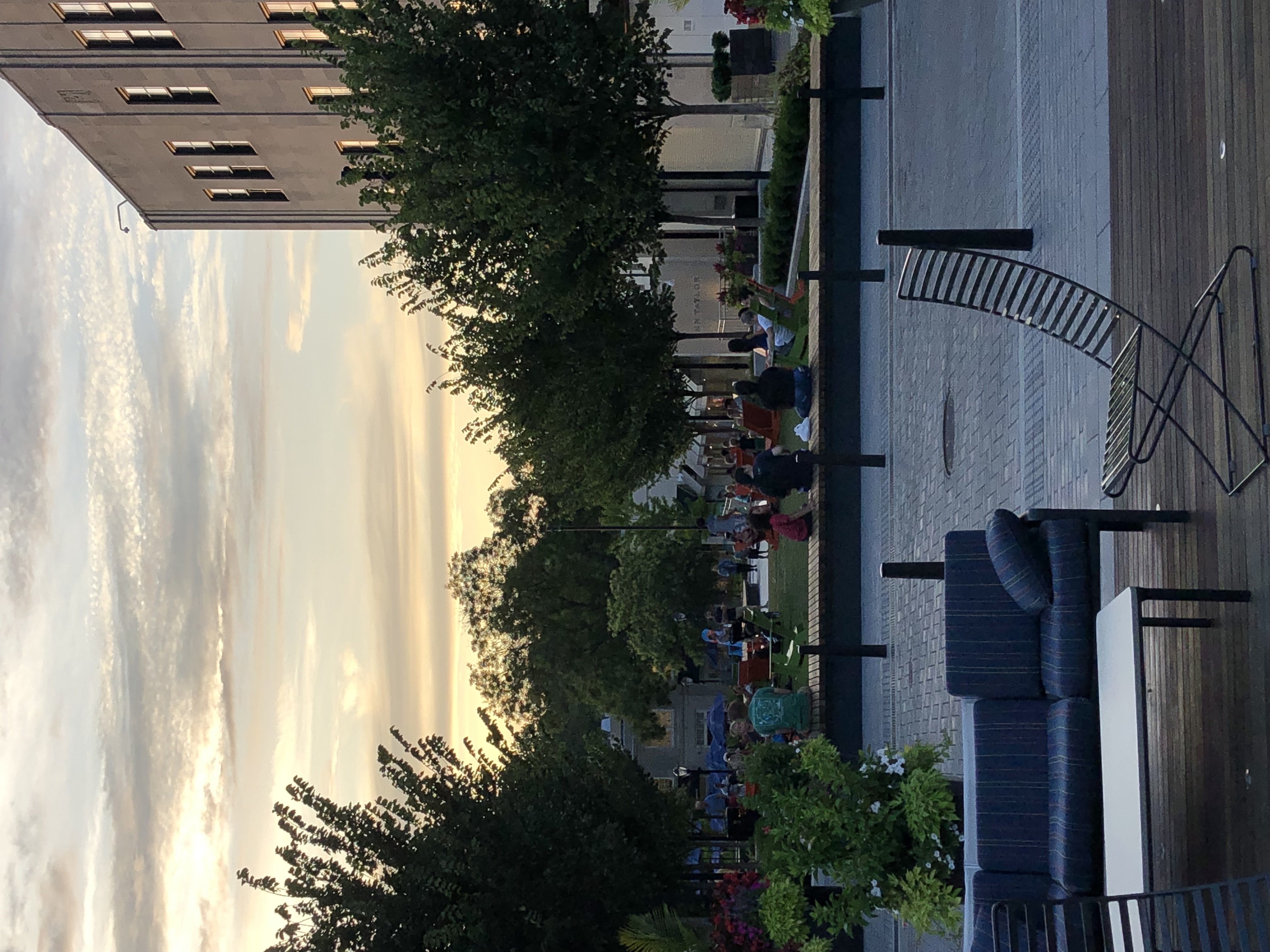 Pedestrians gather in an outdoor plaza lined with trees and seating at dusk.