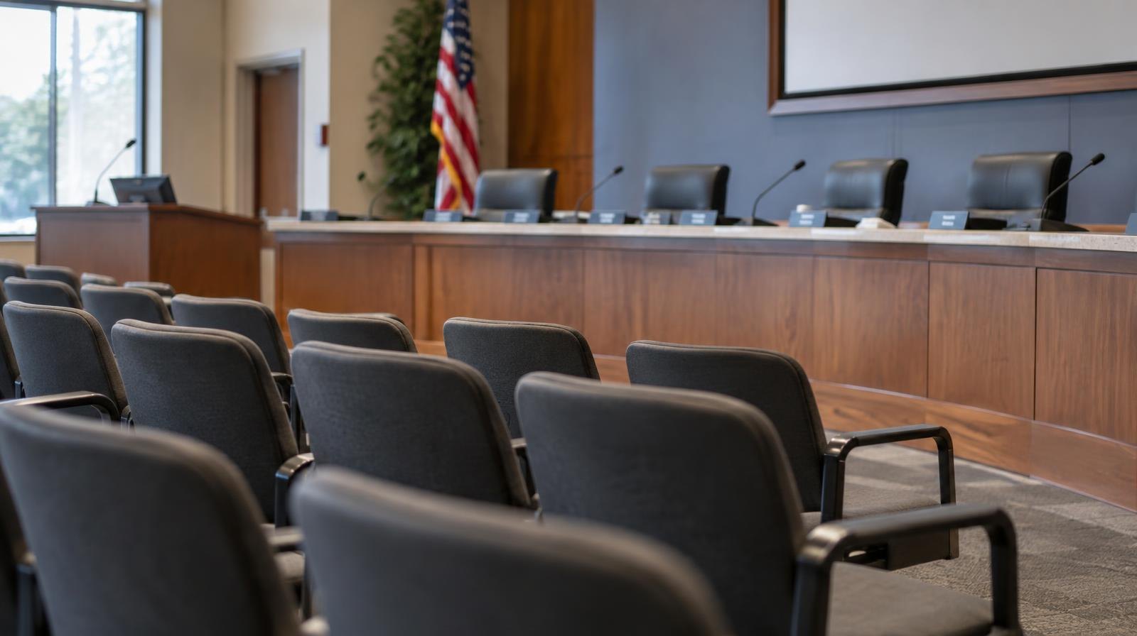 Empty city council chamber with curved dais, microphones, and name placards.
