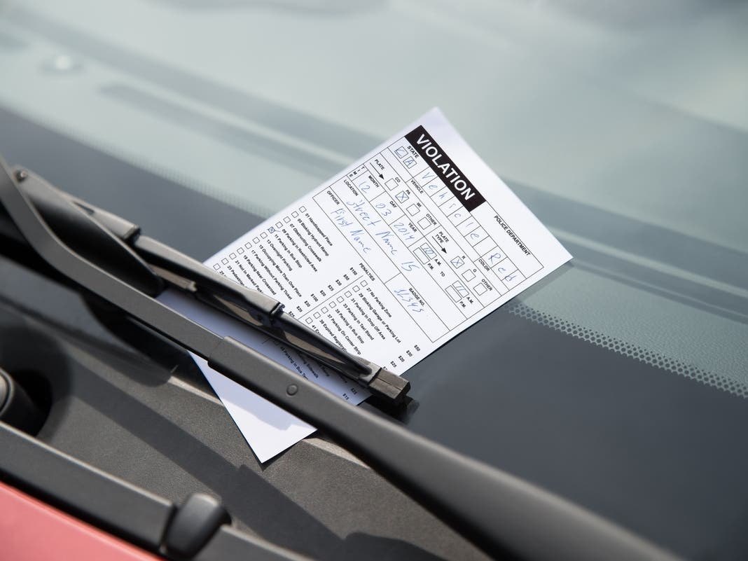 A parking violation ticket placed under a car's windshield wiper.