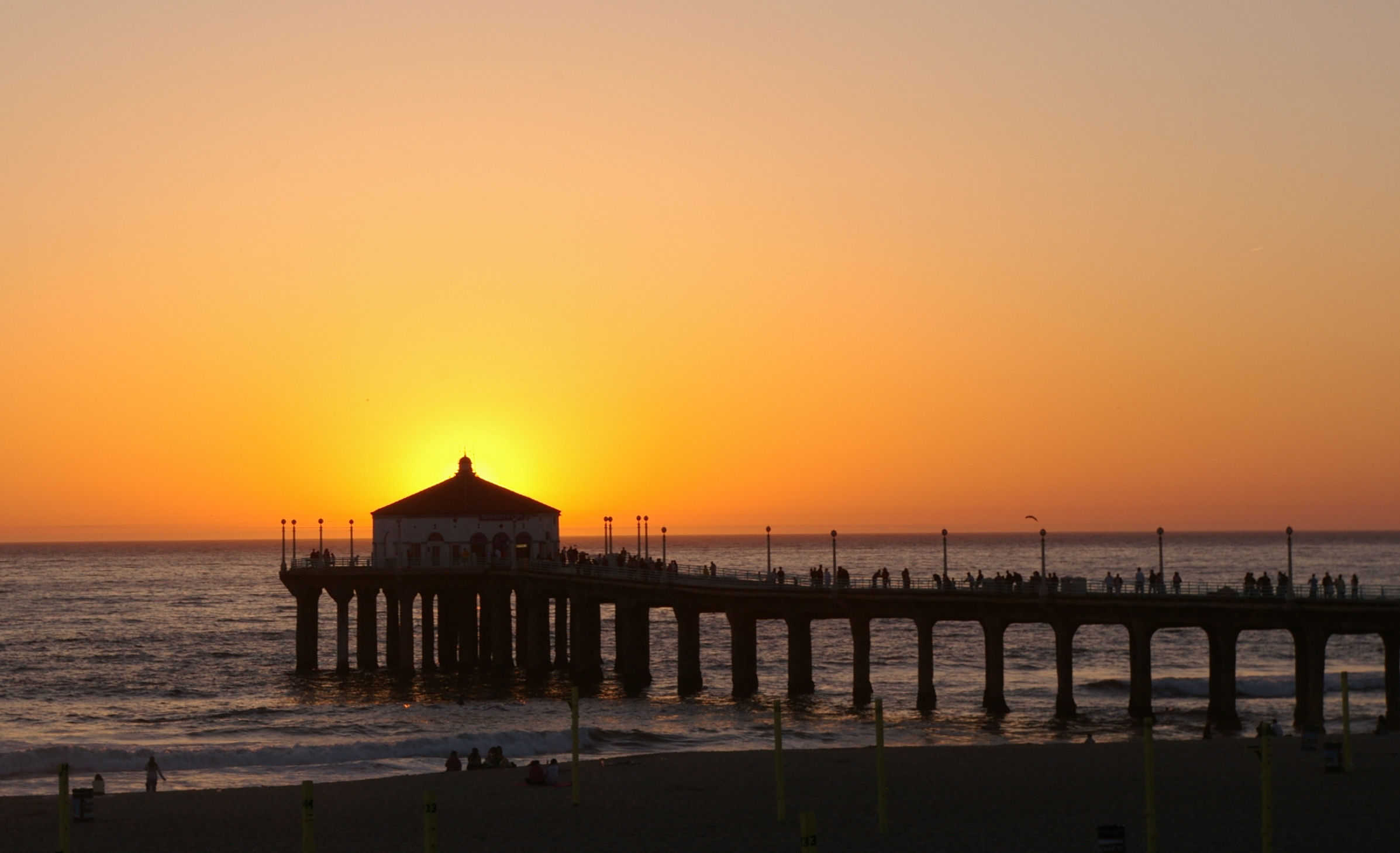 A pier extends into the ocean at sunset with a round building silhouetted at its end.