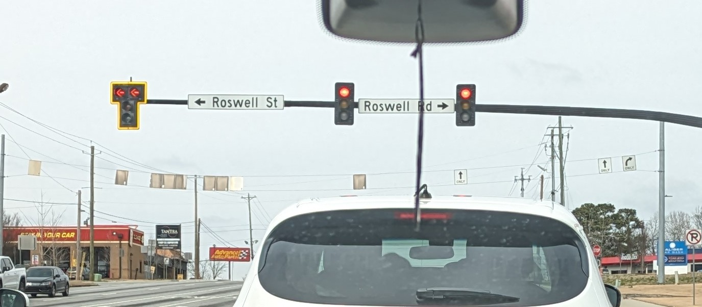 View through a car windshield at a Cobb County, Georgia road intersection with red traffic lights.