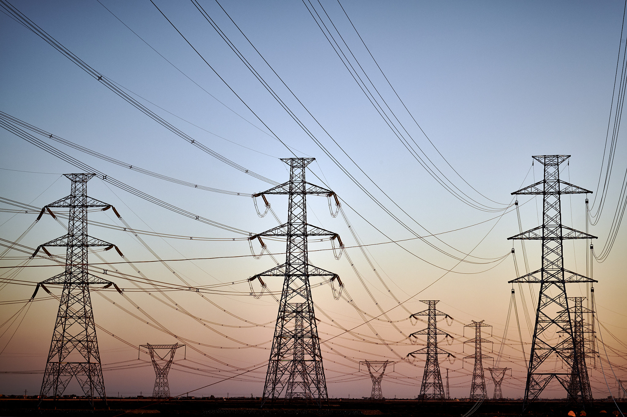 Steel electrical transmission pylons with power lines silhouetted against a twilight sky.