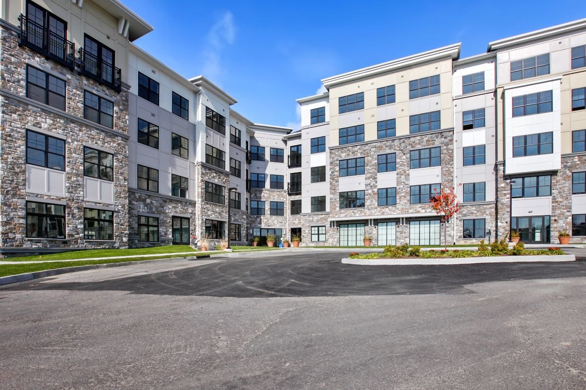 Modern multi-story apartment complex with stone facade, balconies, and curved entrance.
