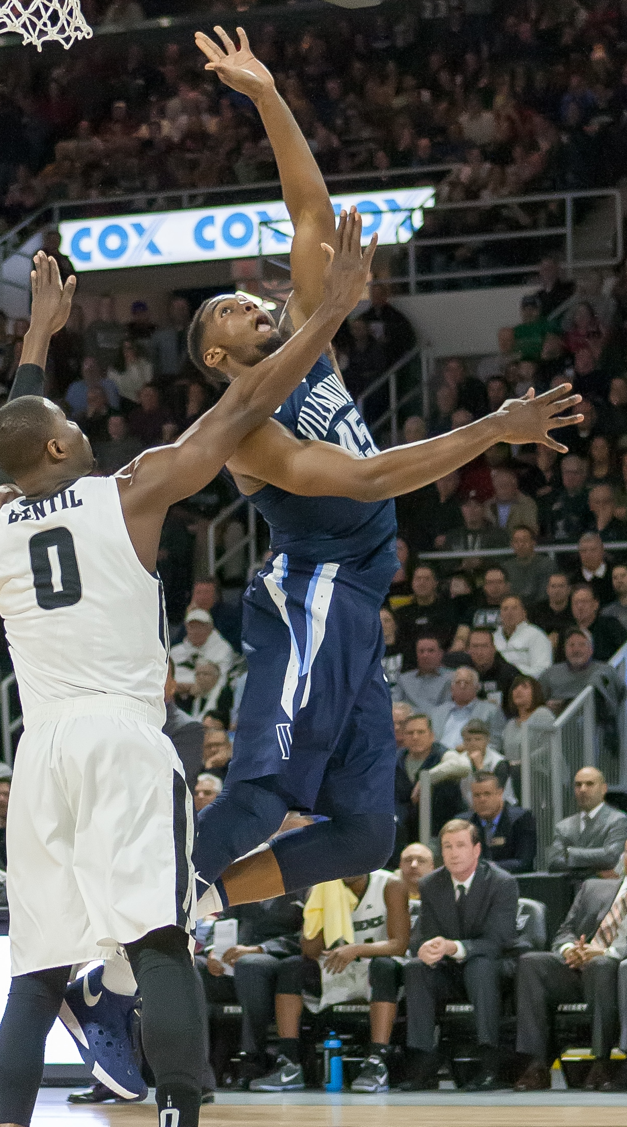 A basketball player in a navy Villanova uniform drives to the basket past a defender.