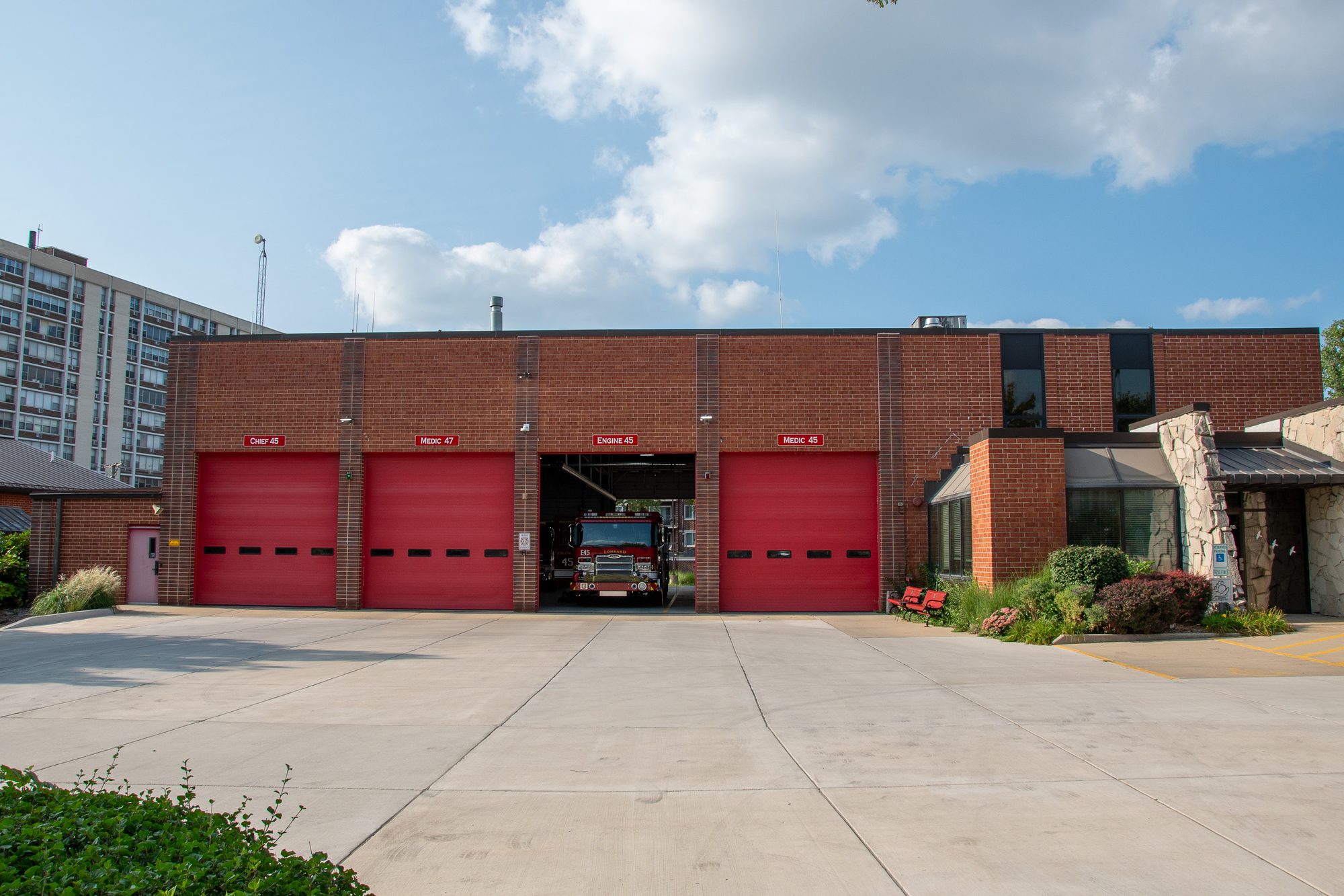 Brick fire station with four red bay doors, one open revealing a fire truck inside.