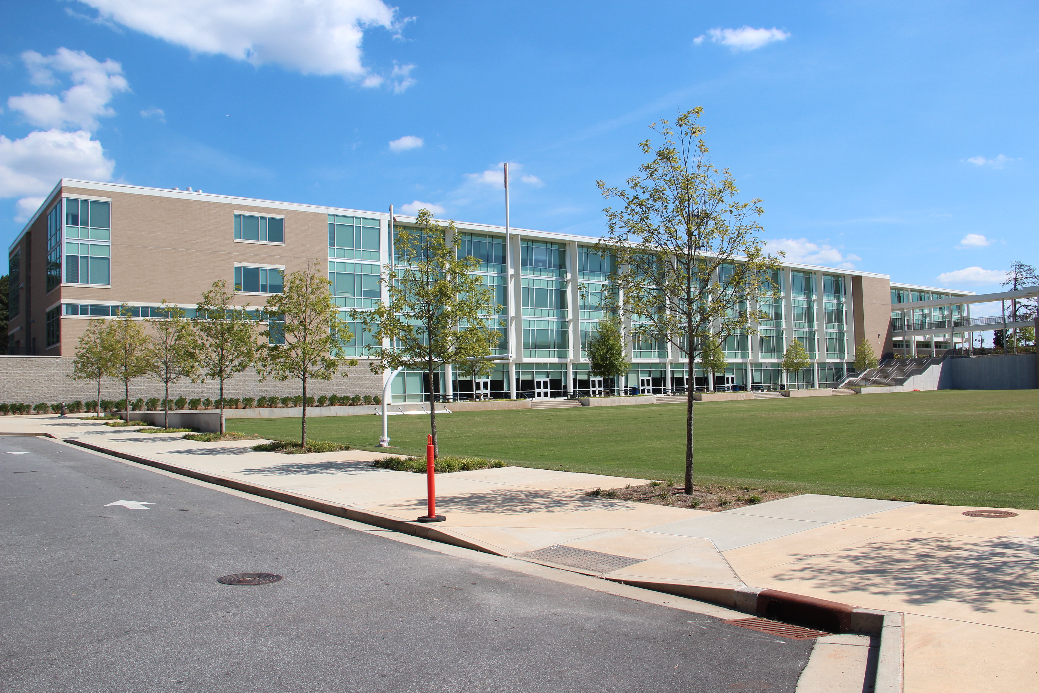 Modern multi-story brick and glass school building with flagpole and manicured lawn.