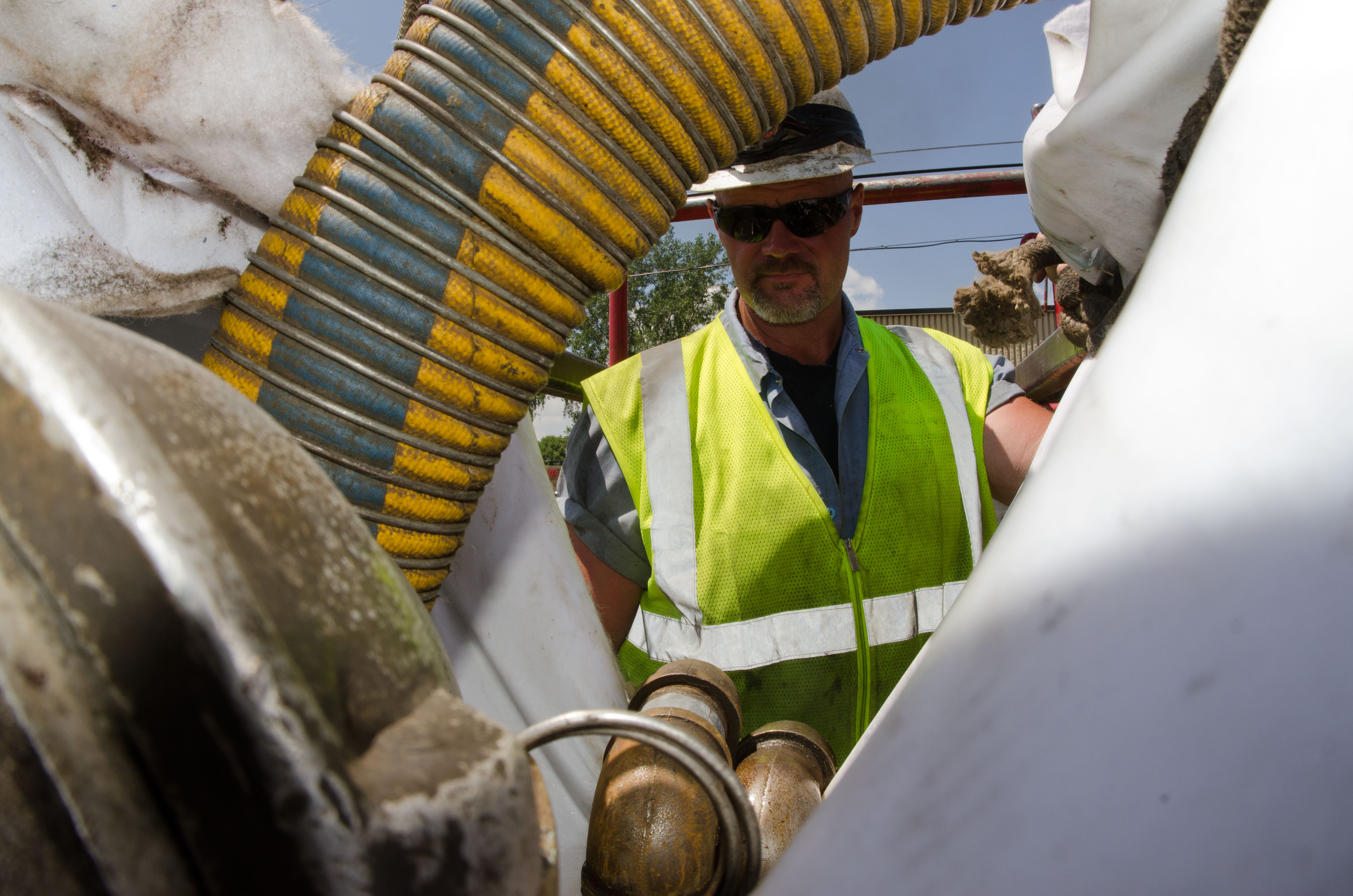 Worker in safety vest stands next to a large flexible sewer liner hose outdoors.