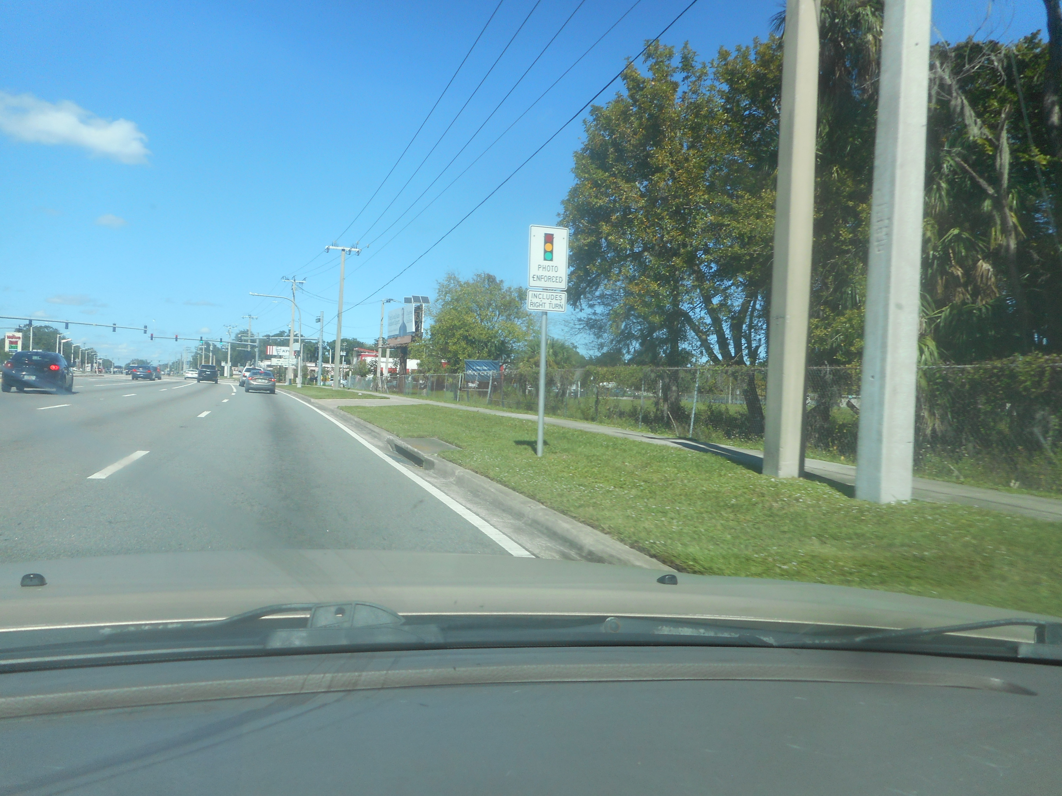 A photo enforcement warning sign mounted on a pole along a multi-lane road.