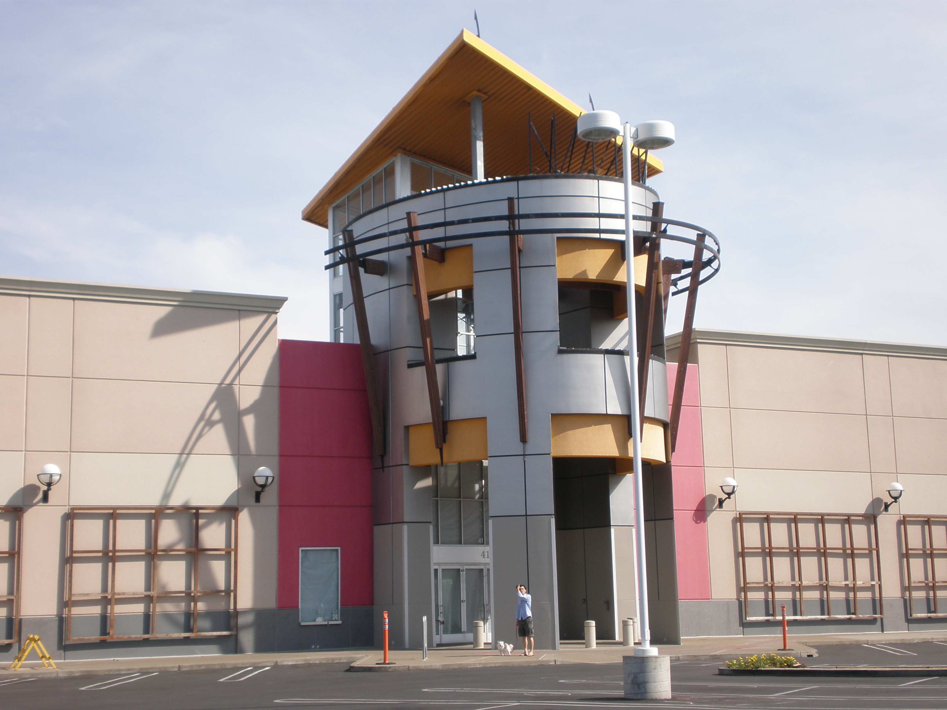 Cylindrical tower entrance at a shopping center, with a yellow roof and metallic cladding.
