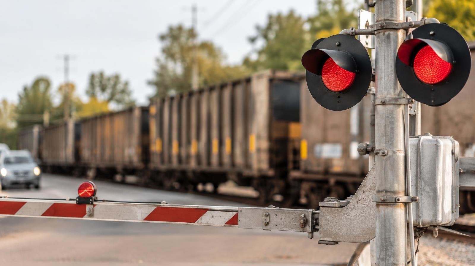 A lowered railroad crossing gate with red flashing lights and a stopped freight train behind it.