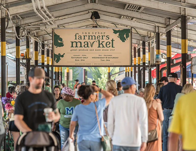 Visitors walk through the covered Ann Arbor Farmers Market beneath a large market sign.