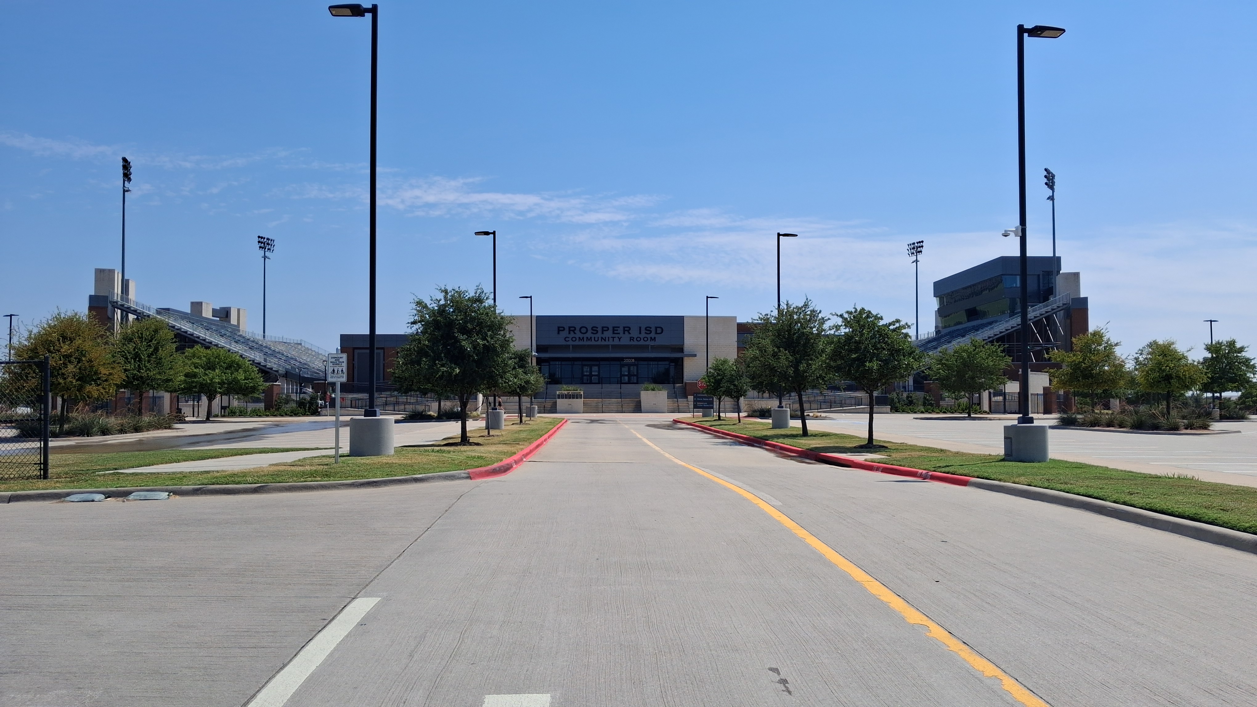 Entrance road leading to a building marked Prosper ISD under a clear blue sky.