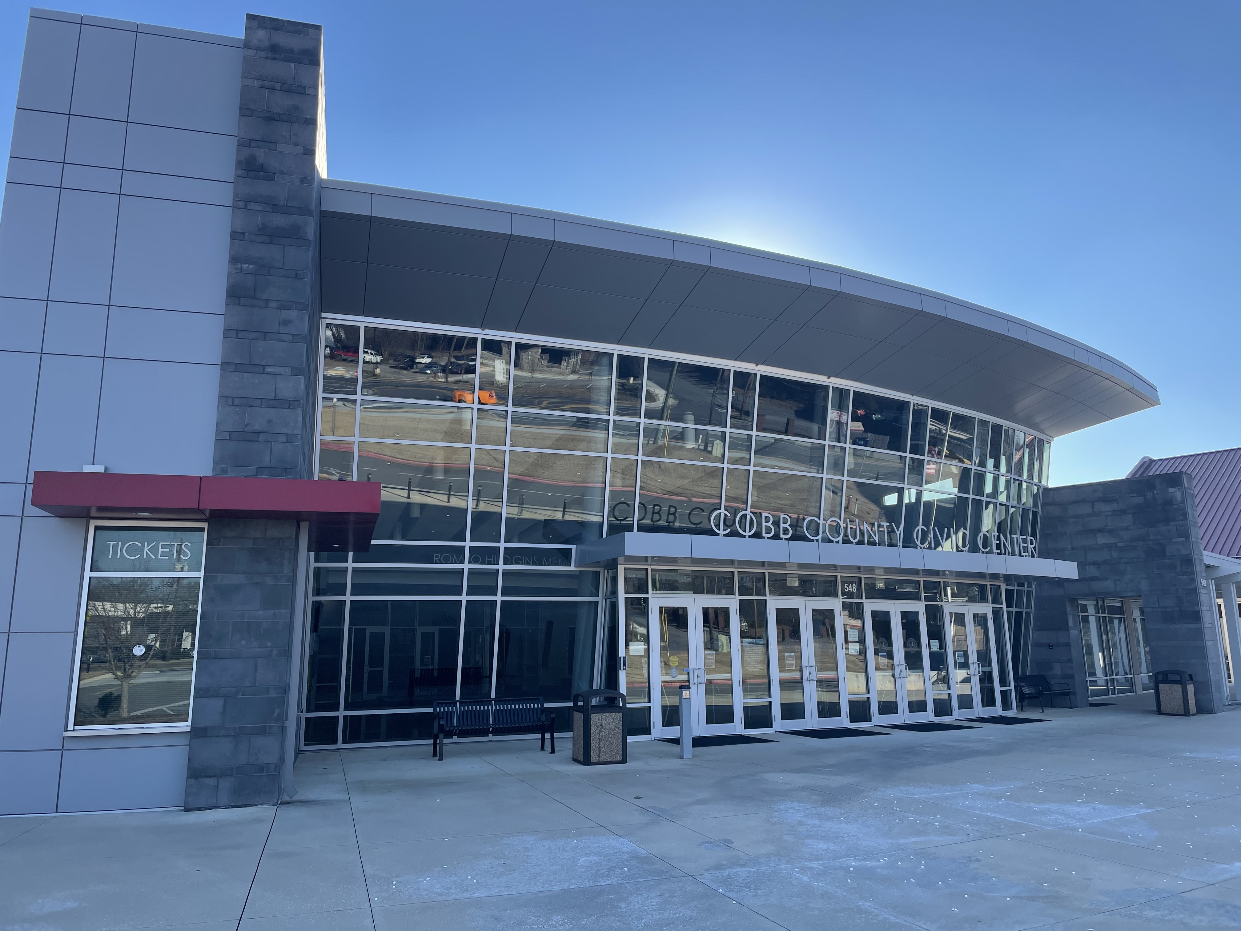 Exterior of a building with a curved glass facade and entrance plaza on a sunny day.