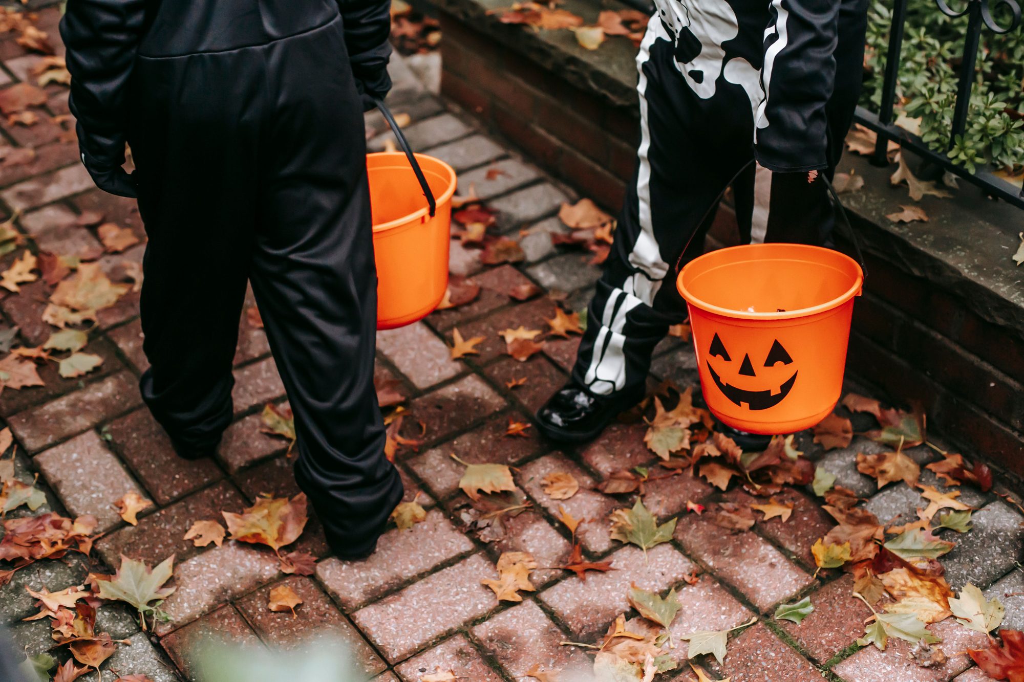 children in black skeleton costumes with orange buckets trick or treating in Halloween in day