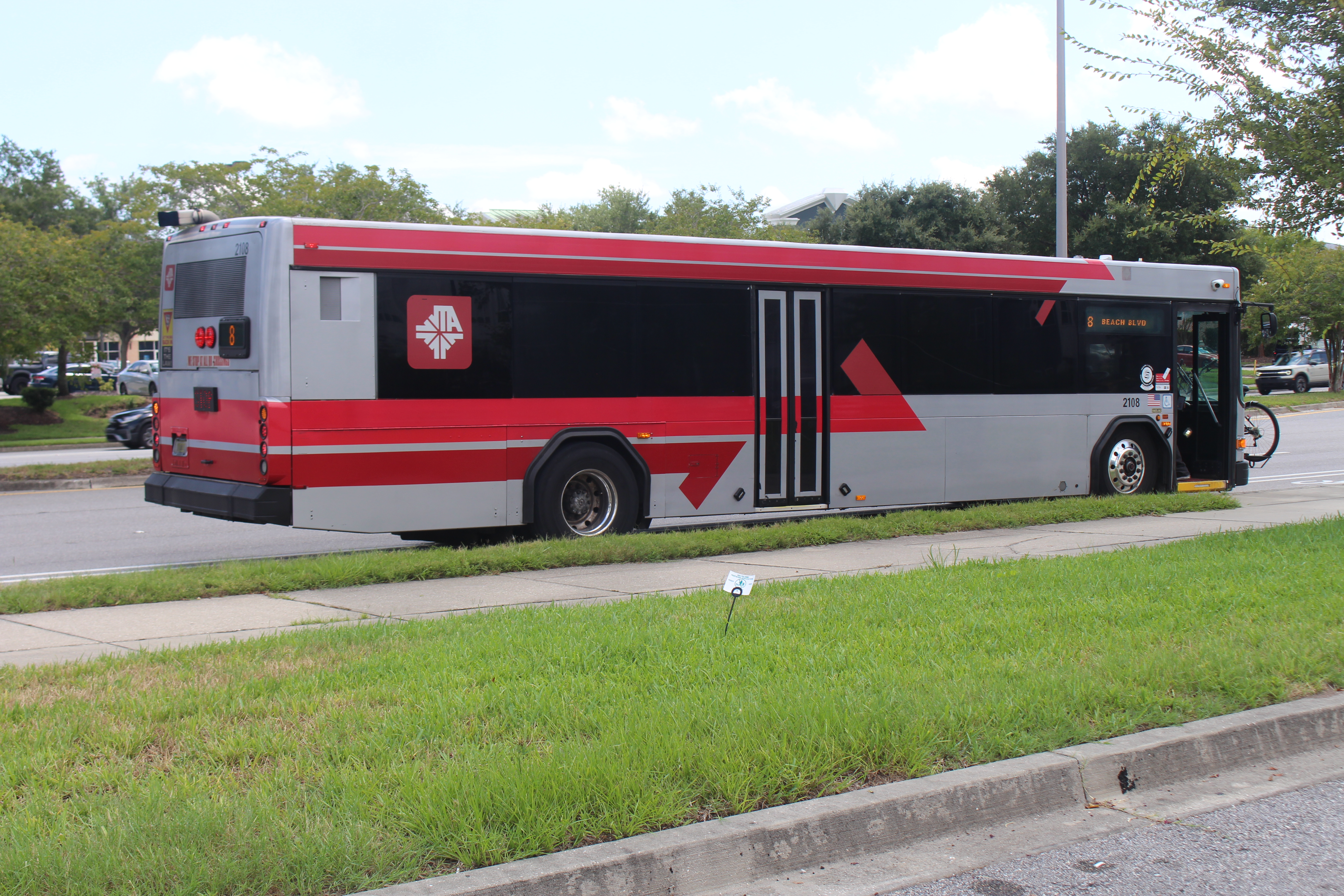 A red, black, and gray public transit bus stopped at a roadside bus stop.