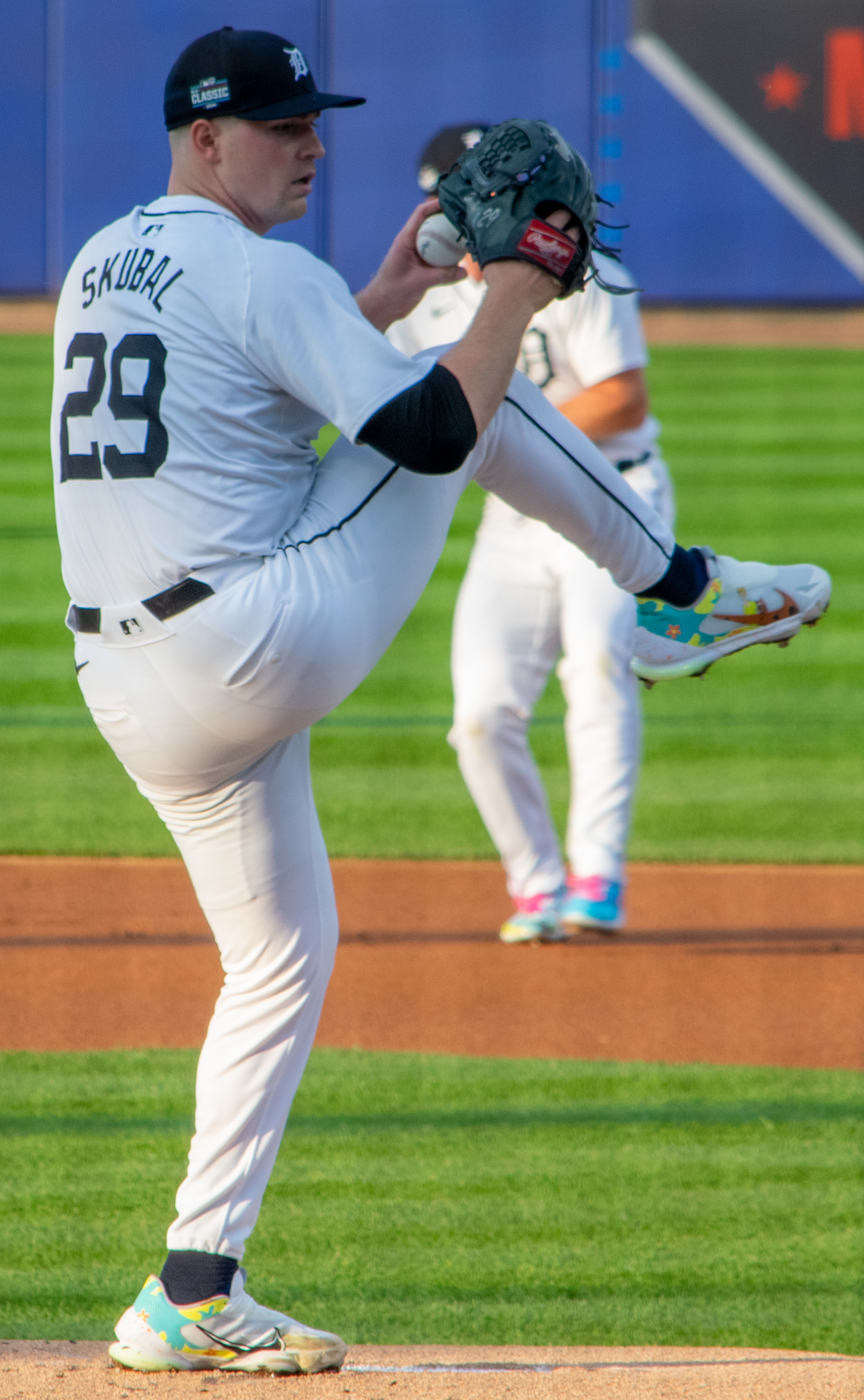 Baseball pitcher in white uniform number 29 mid-windup with leg raised high.