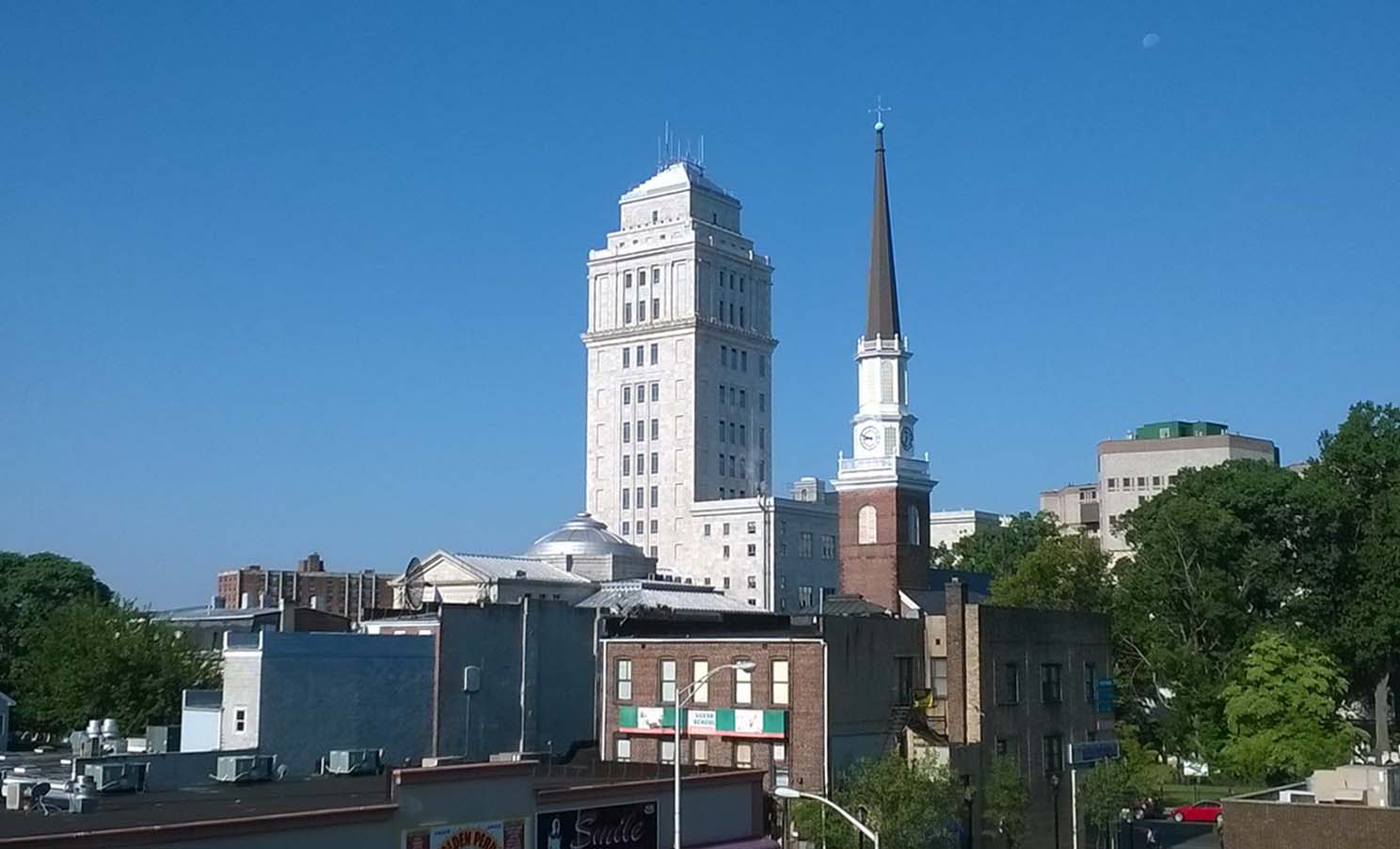 Aerial view of a tall white government courthouse tower amid downtown buildings under a clear blue sky.