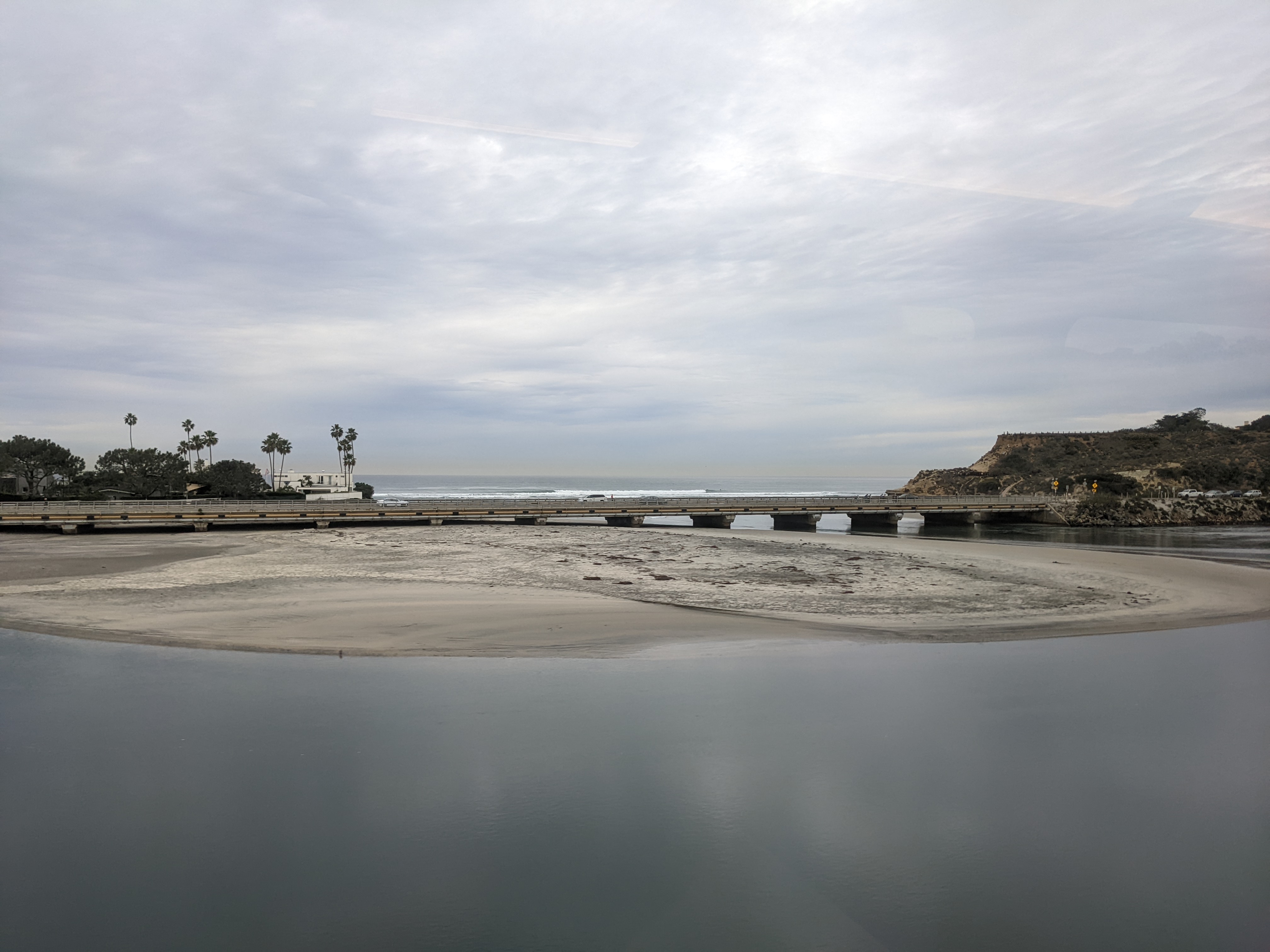 Low bridge spanning a calm coastal river mouth with bluffs and ocean beyond.
