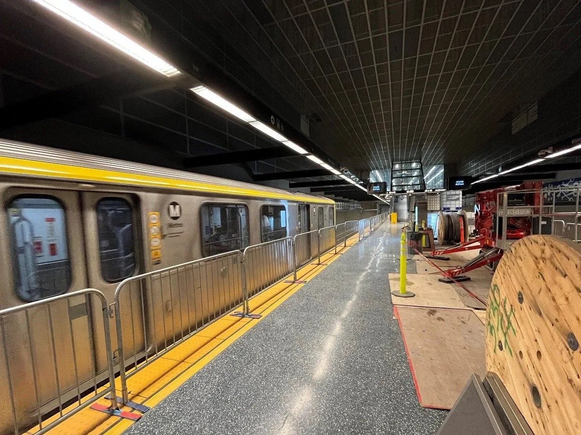 A Metro rail train arriving at an underground station platform with metal barriers along the edge.