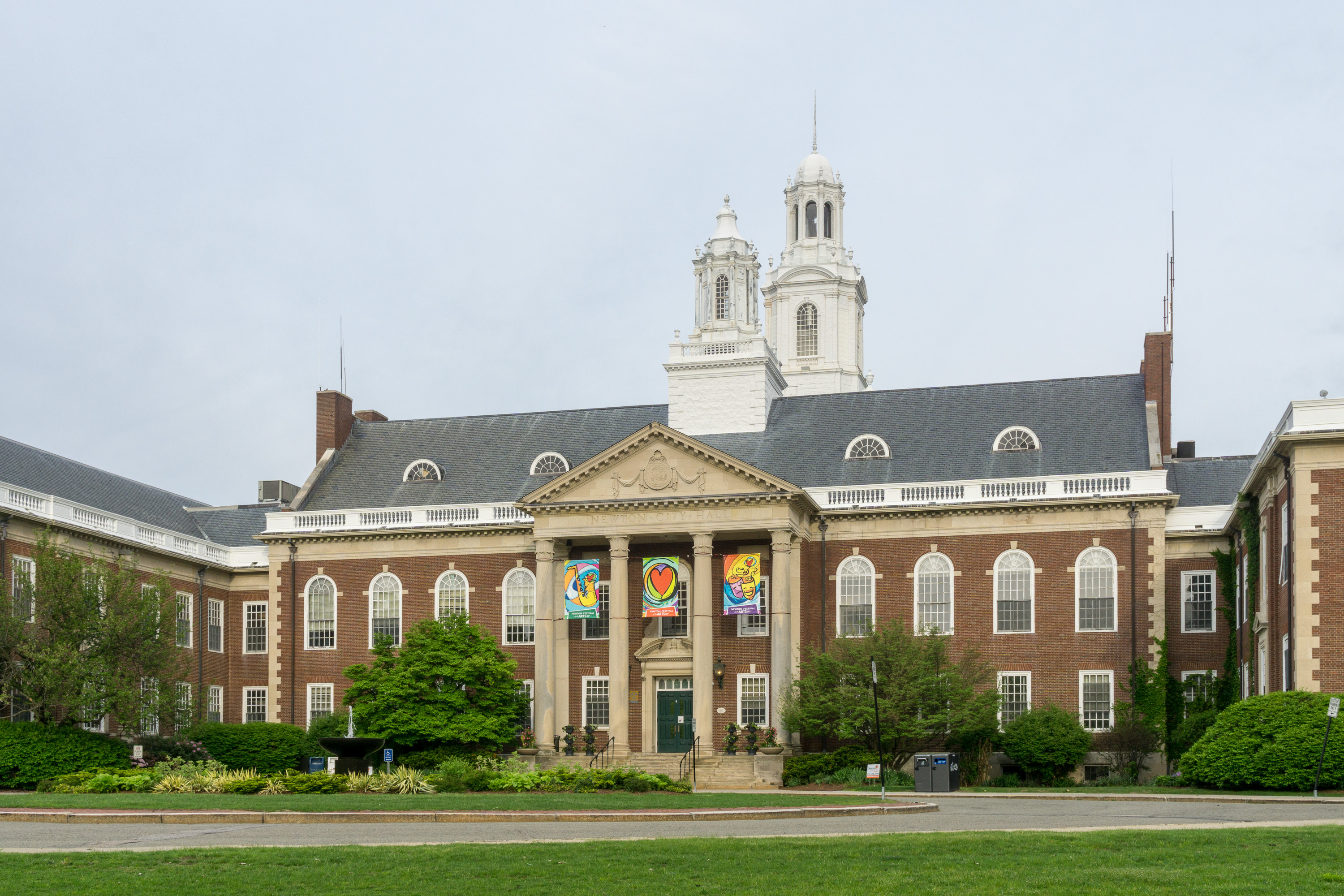 Red-brick Newton City Hall with white cupolas and colorful banners on the facade.