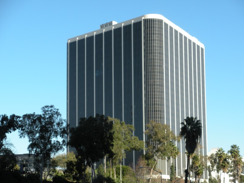 Tall modernist office tower with white columns and dark glass panels, flanked by palm trees.