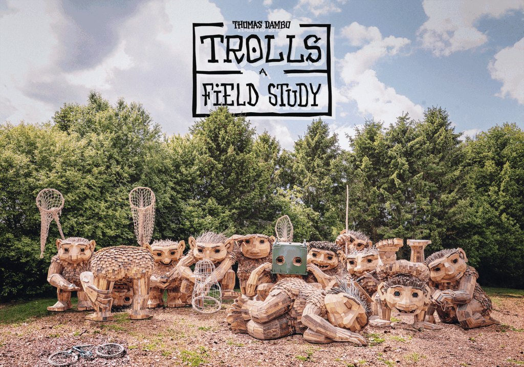 Several large wooden troll sculptures made from reclaimed branches stand outdoors among trees.