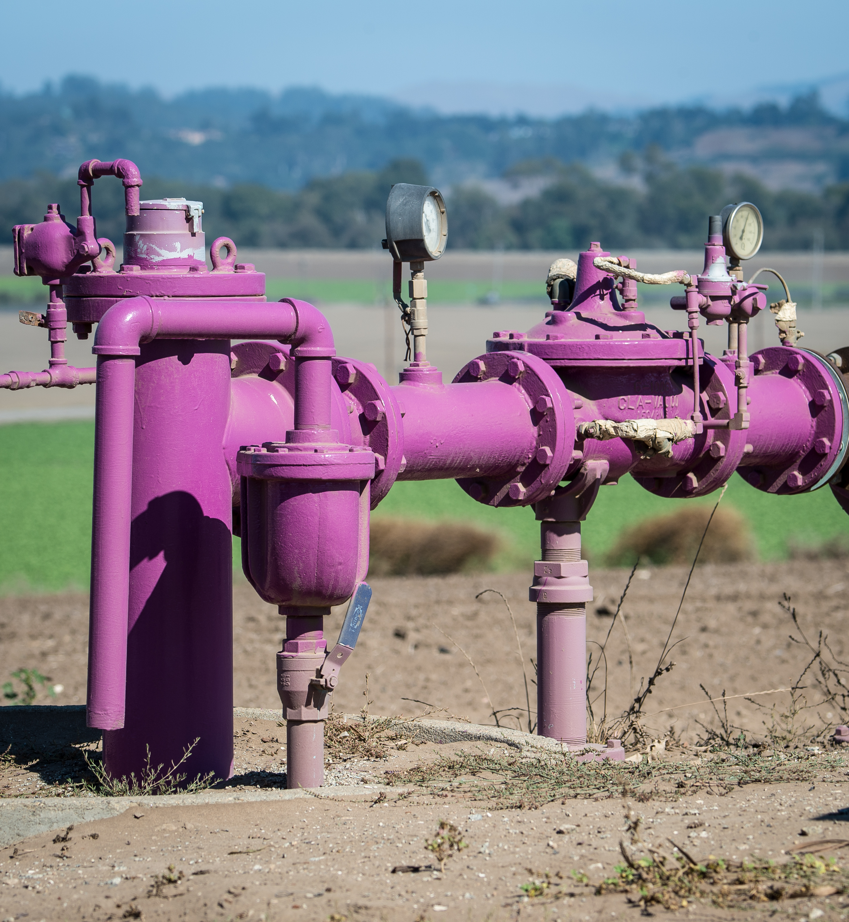 Purple industrial water pipes with valves and pressure gauges at an outdoor water recycling facility.