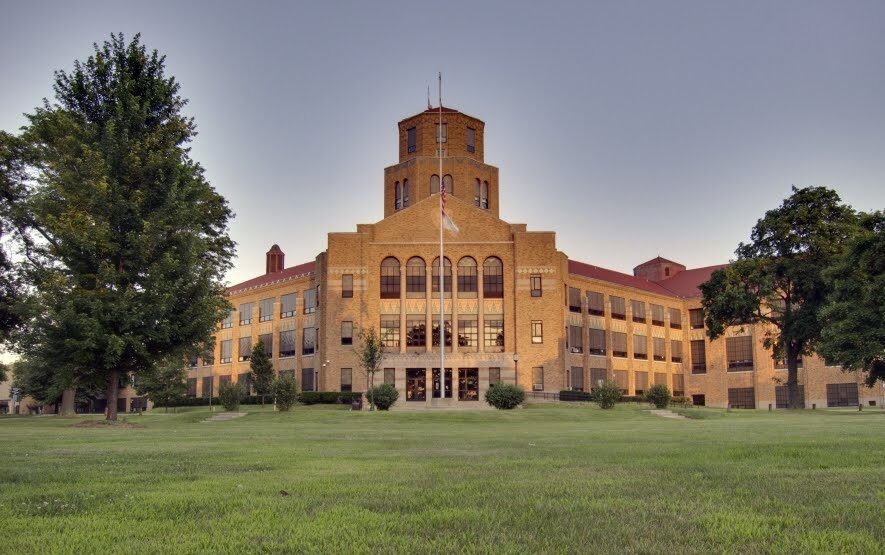 Exterior of a large brick high school building with arched windows and a central tower.