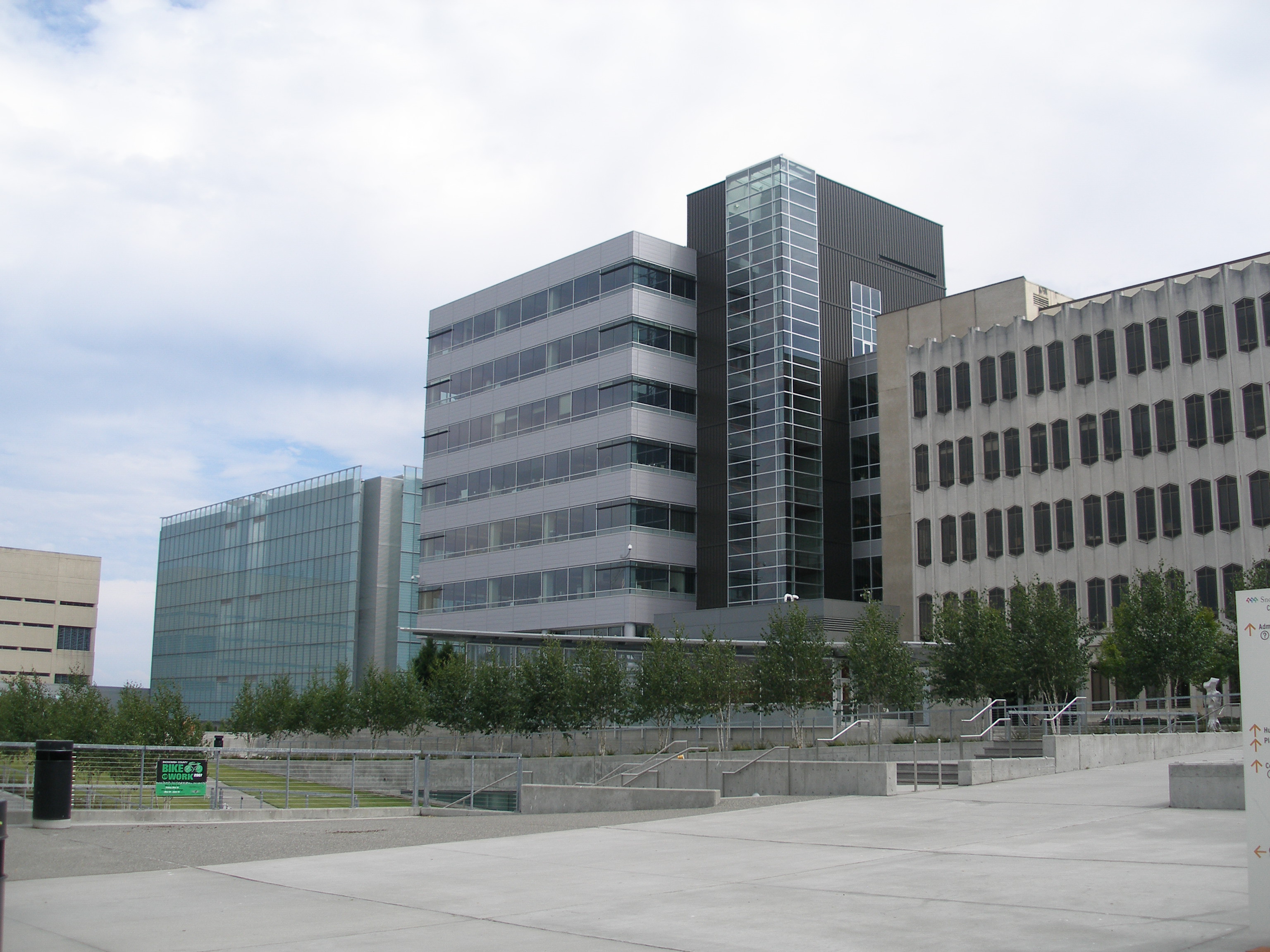 Multi-story government office buildings on a paved campus plaza under a partly cloudy sky.