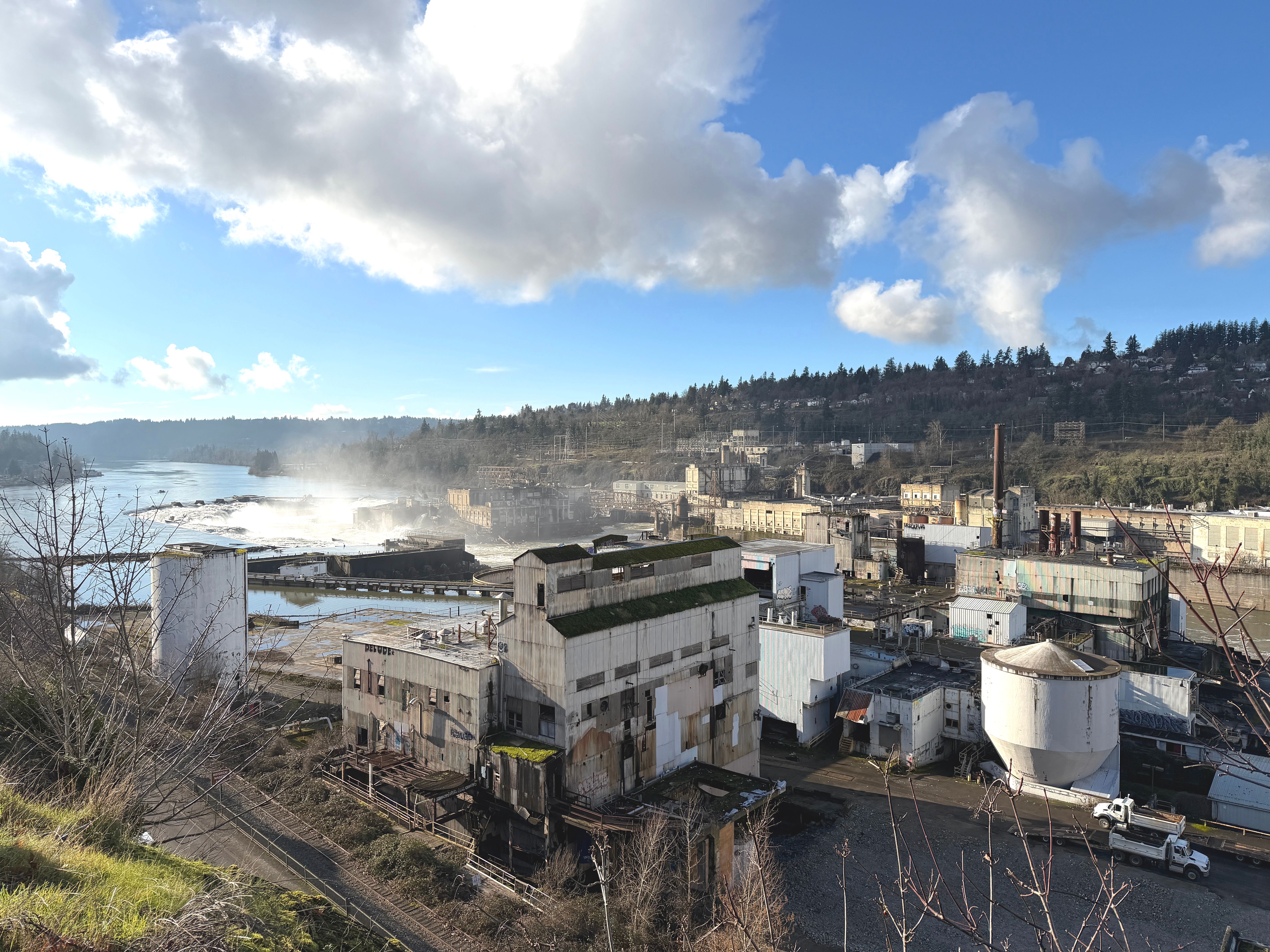 Abandoned industrial buildings line the Willamette River with mist rising from nearby falls.
