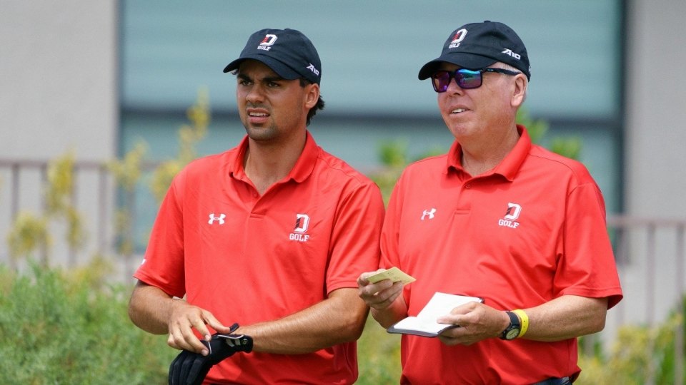 Two men in matching red Davidson Golf polo shirts review notes on a golf course.