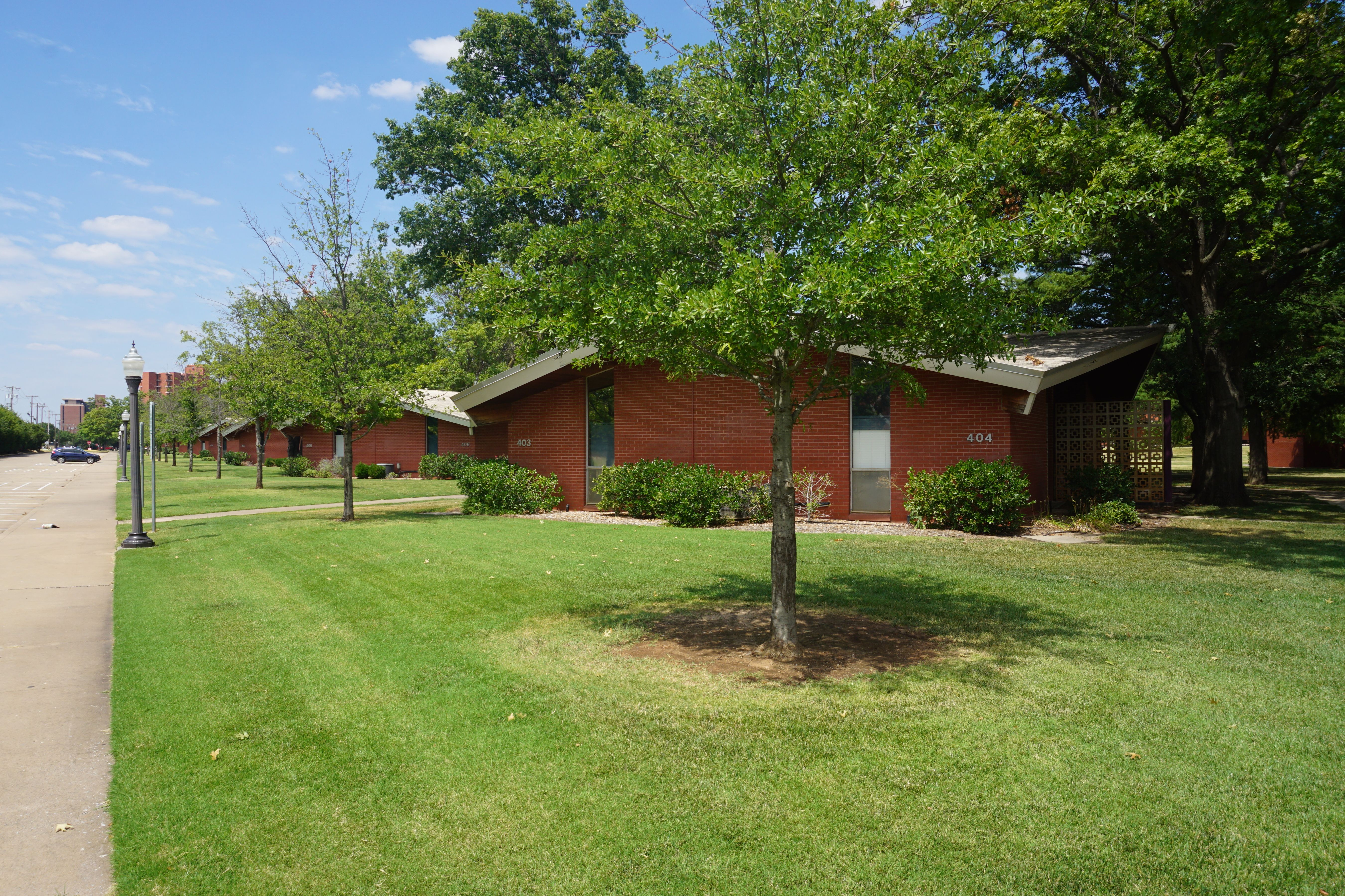 A row of single-story brick residential buildings on a tree-lined campus street.