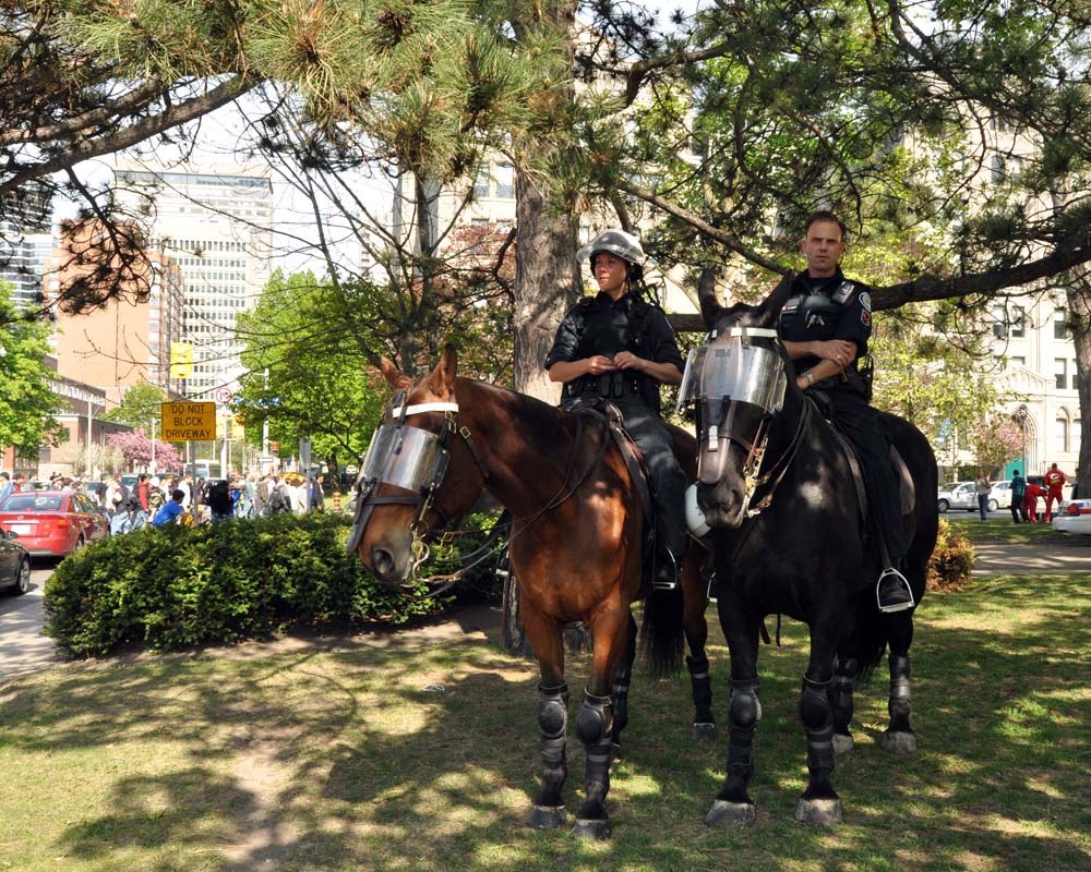 Two officers on horseback in riot gear stand near a crowd on a city street.