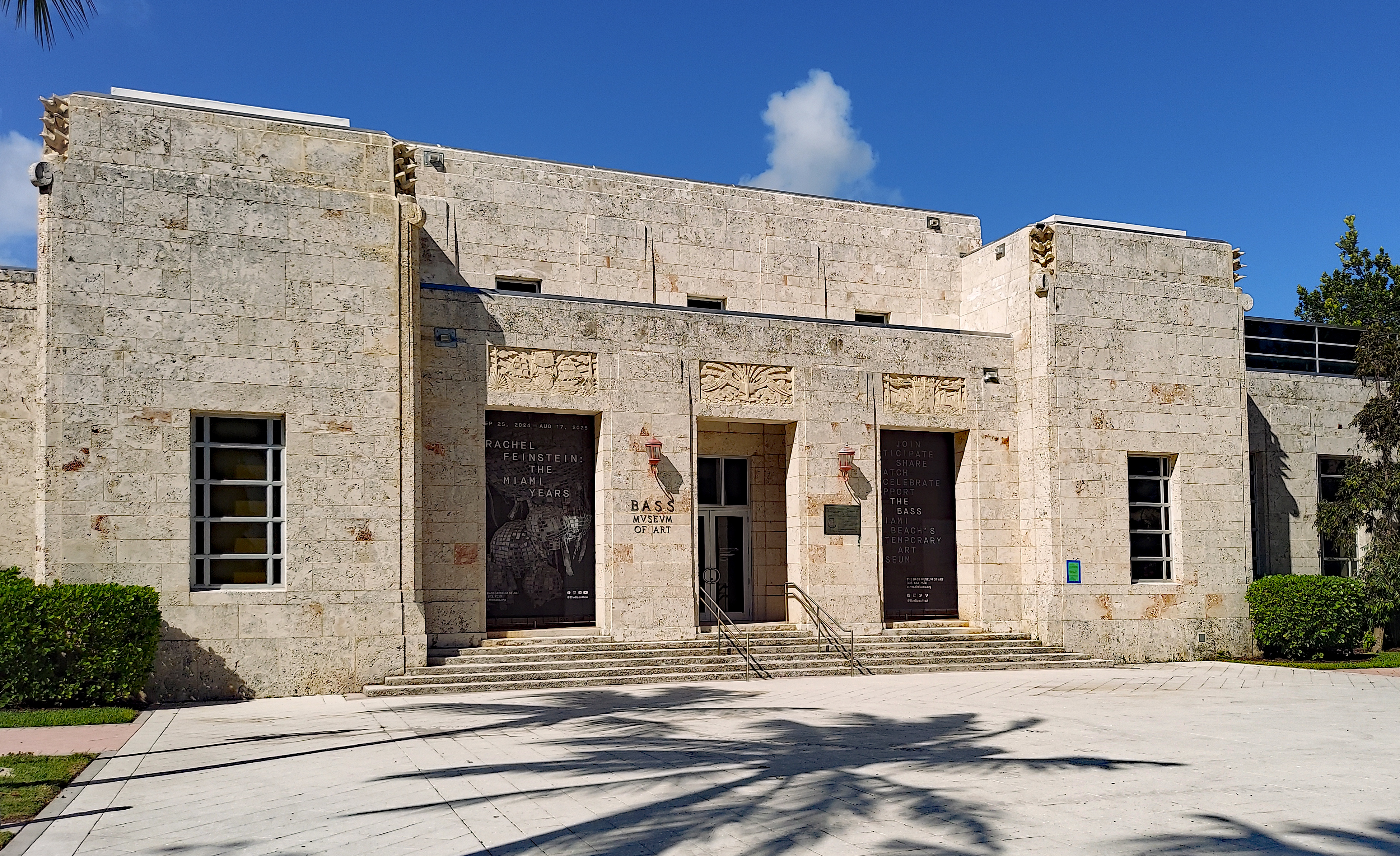 Limestone Art Deco museum building with steps, decorative carvings, and palm trees.