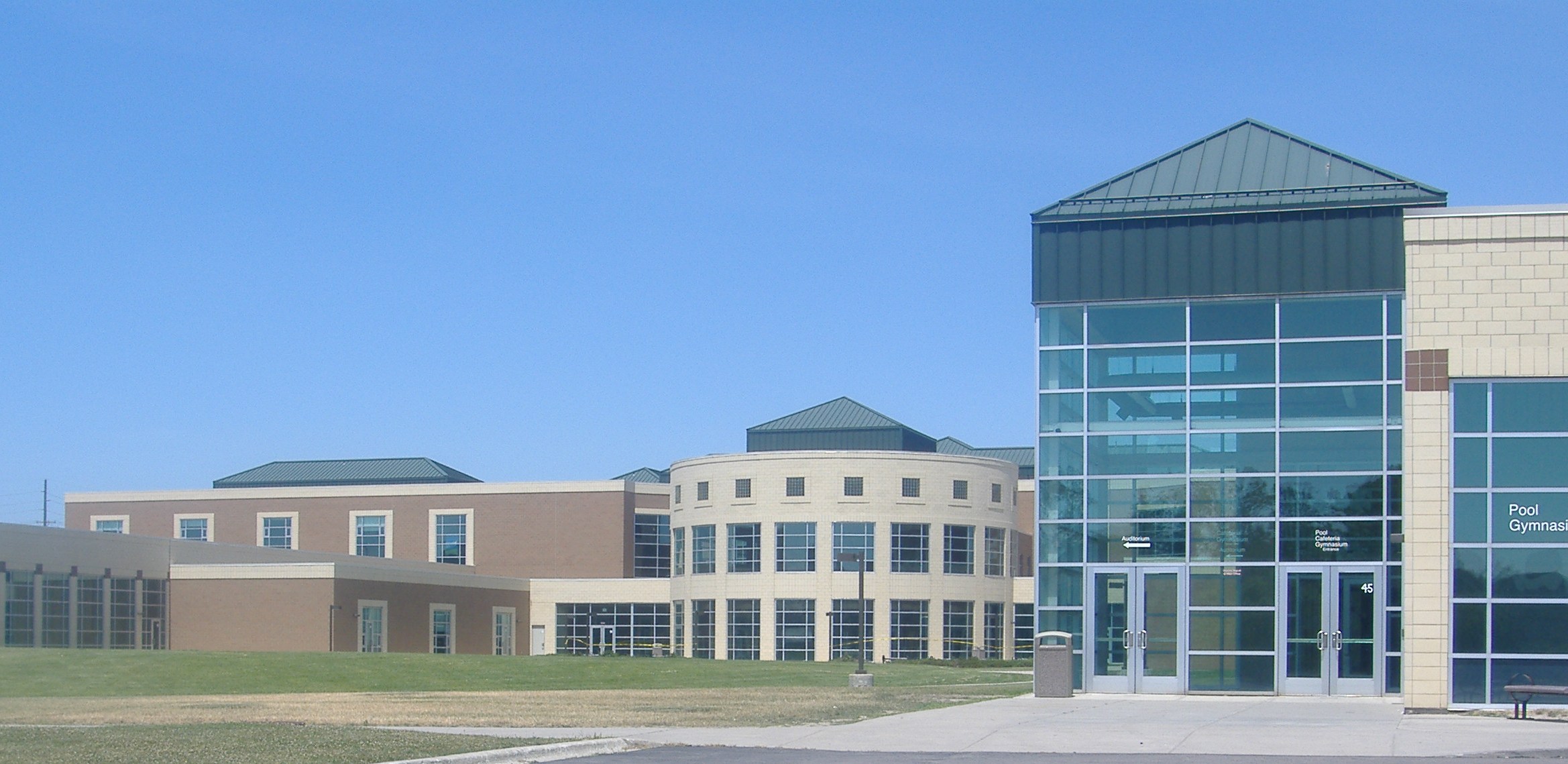 Exterior of a large modern brick and glass high school building under a clear blue sky.