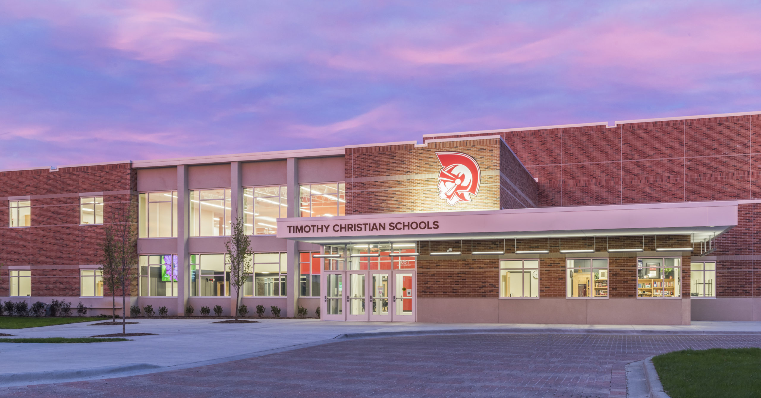 Brick school building exterior at dusk with illuminated entrance and school name on facade.