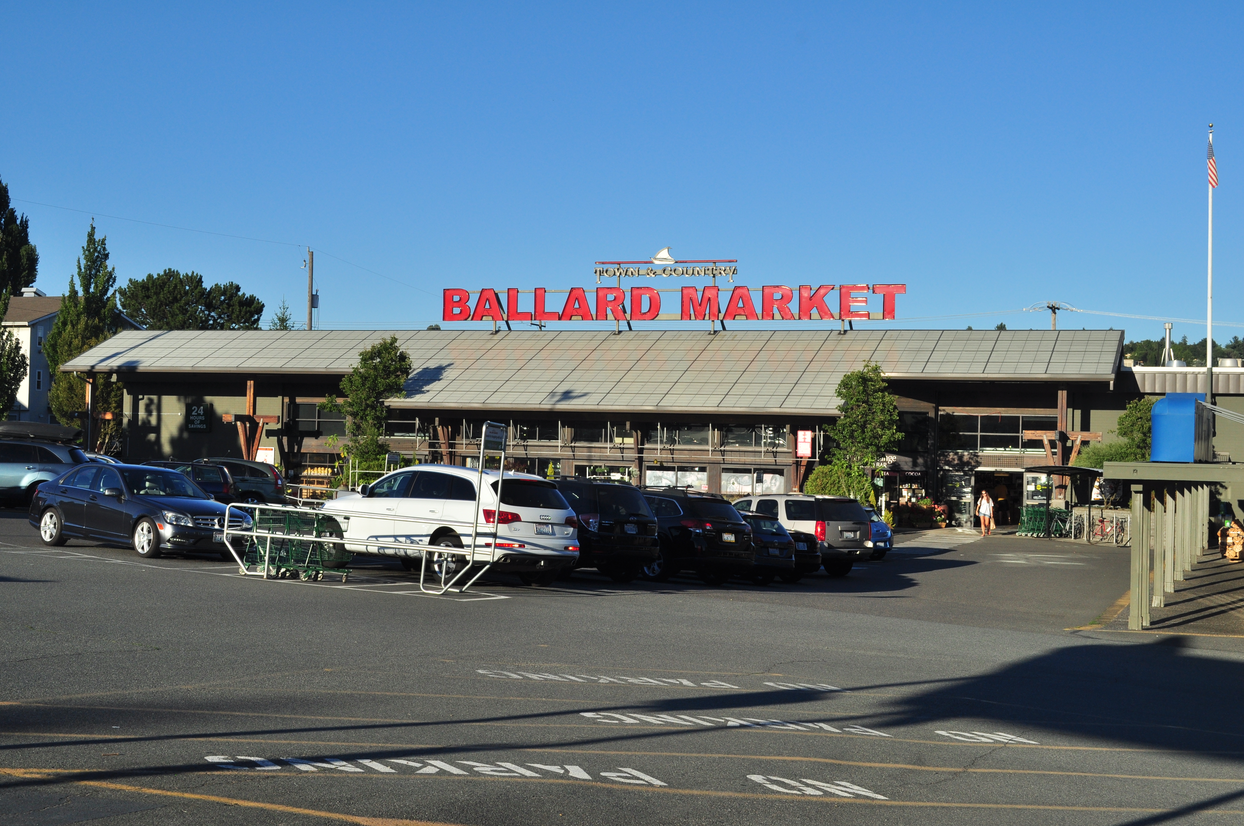 Grocery store exterior with a large red sign reading 'Ballard Market' and a full parking lot.