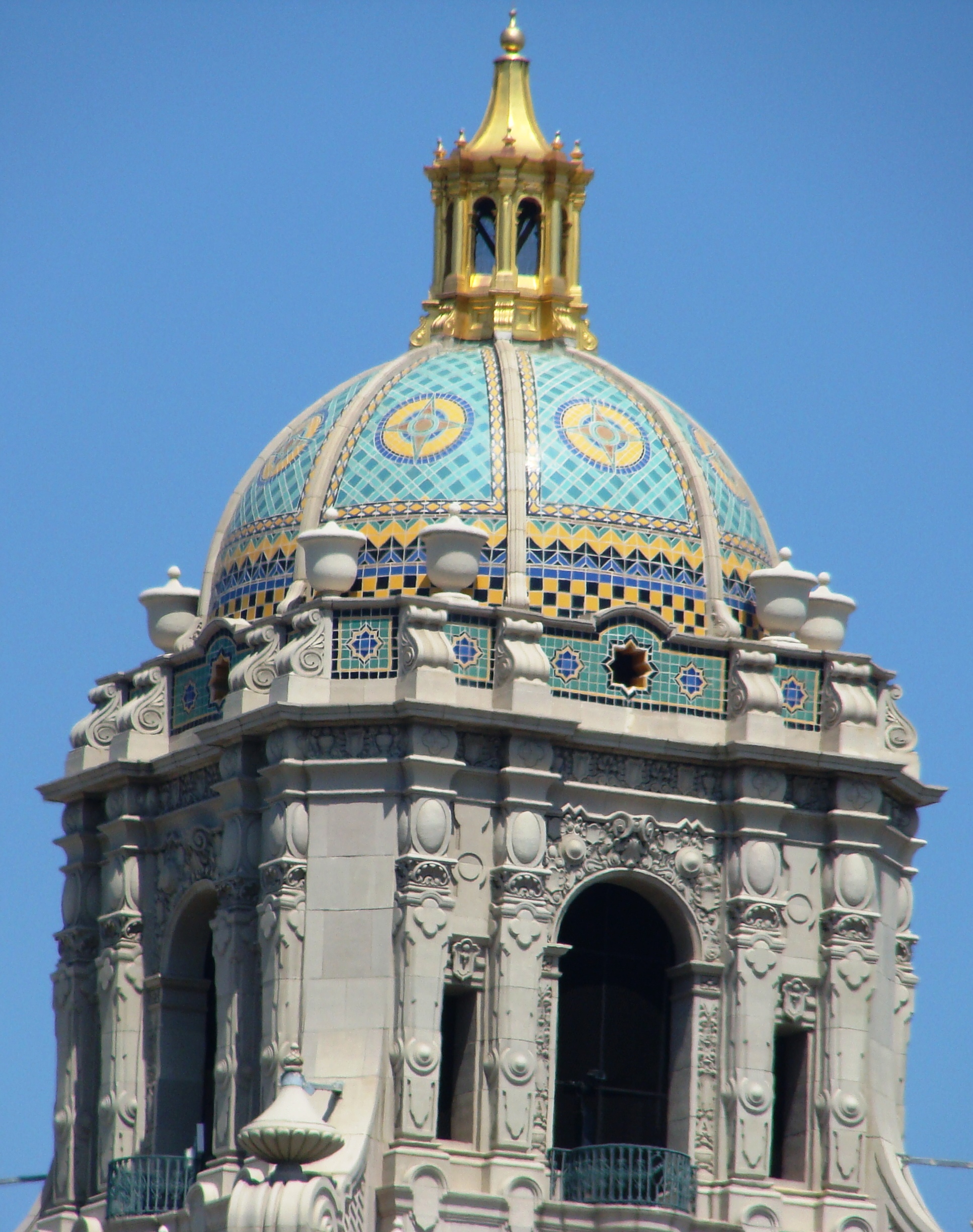 Low-angle view of Beverly Hills City Hall's colorful mosaic dome and gilded cupola against blue sky.