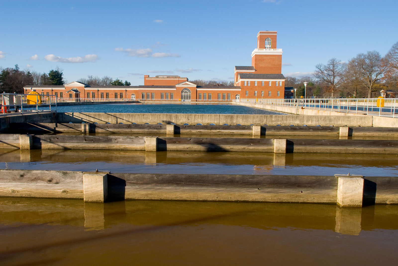 Water treatment facility with concrete settling basins and a brick clock tower building.