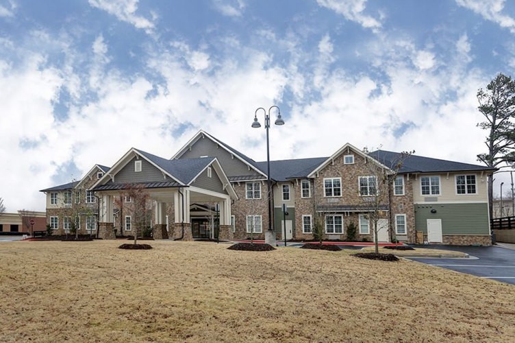 Exterior of a large multi-story assisted living facility with stone and siding, covered entrance portico, and landscaped lawn.