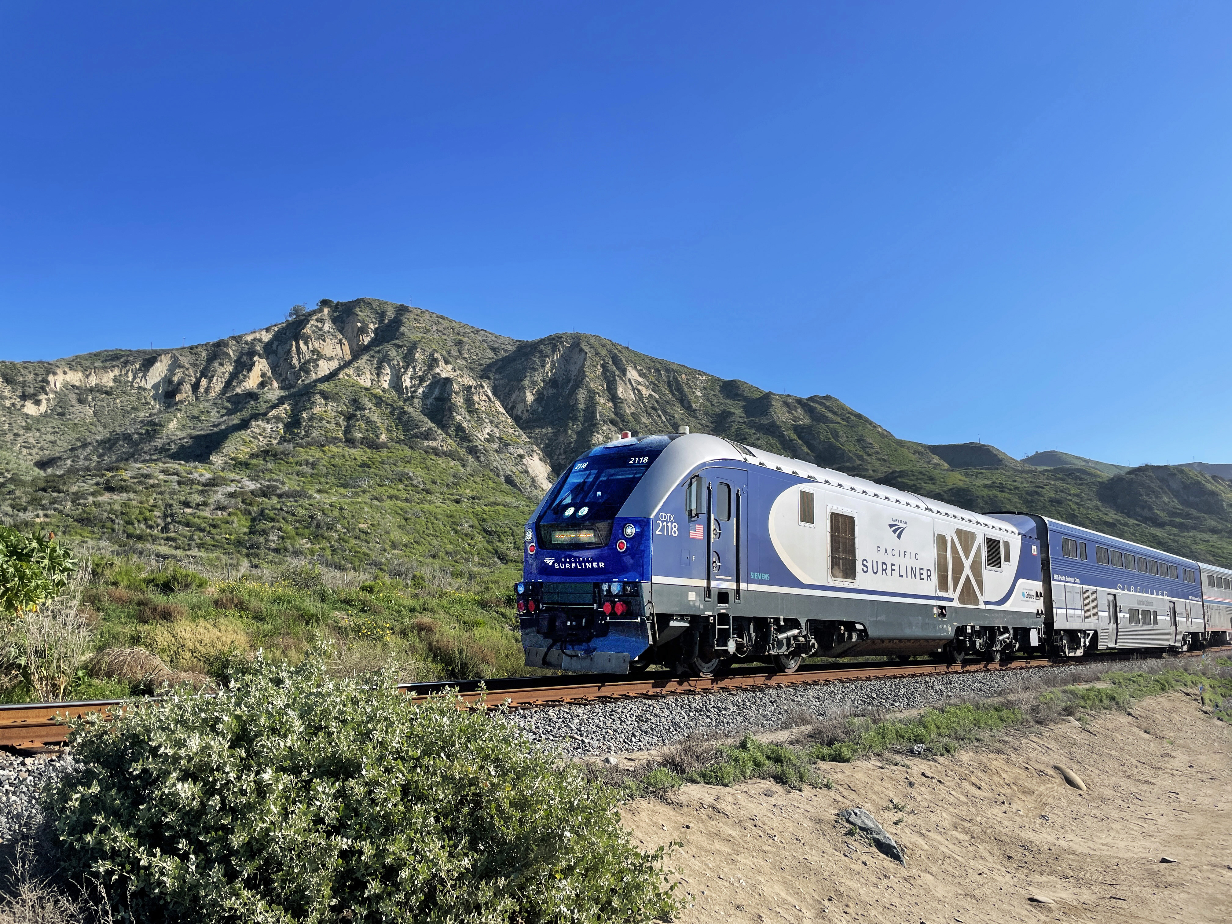 Blue and silver Amtrak Pacific Surfliner locomotive moving along a single-track rail line.