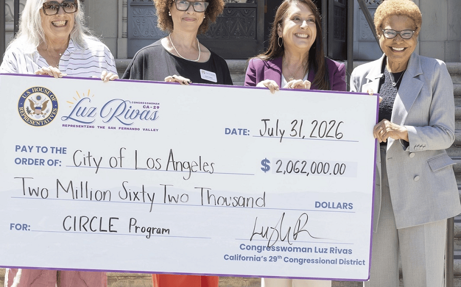 Four women hold an oversized ceremonial check for over two million dollars outdoors.