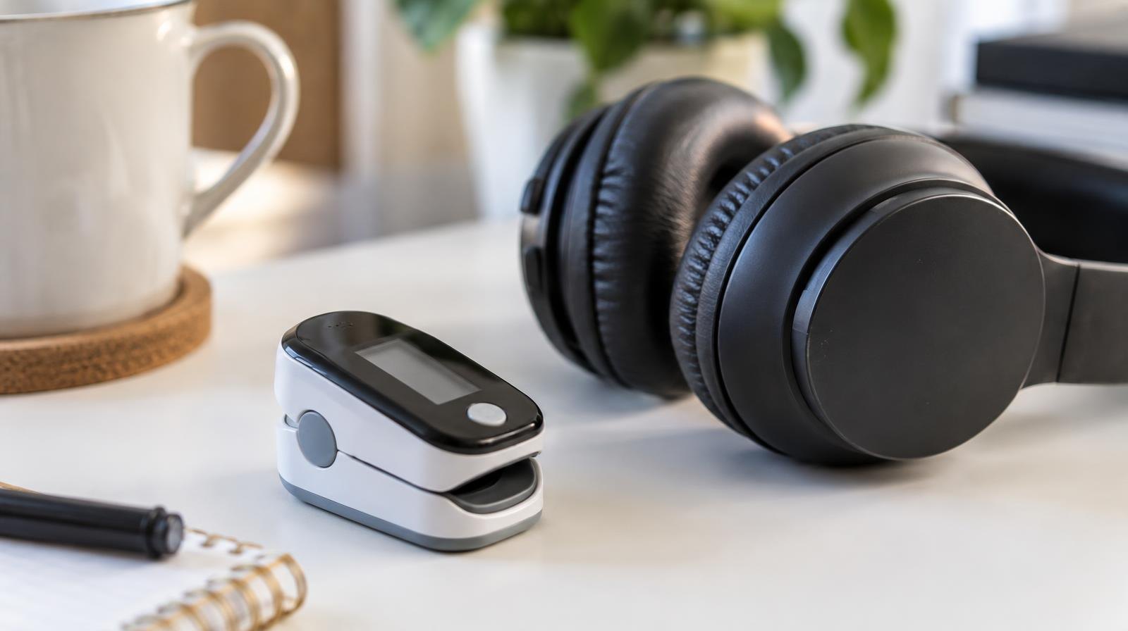 A small finger-clip sensor resting beside over-ear headphones on a white surface.