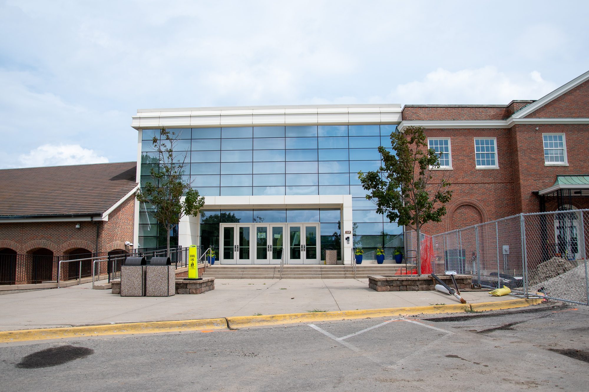 Modern glass school entrance flanked by brick wings with construction fencing alongside.