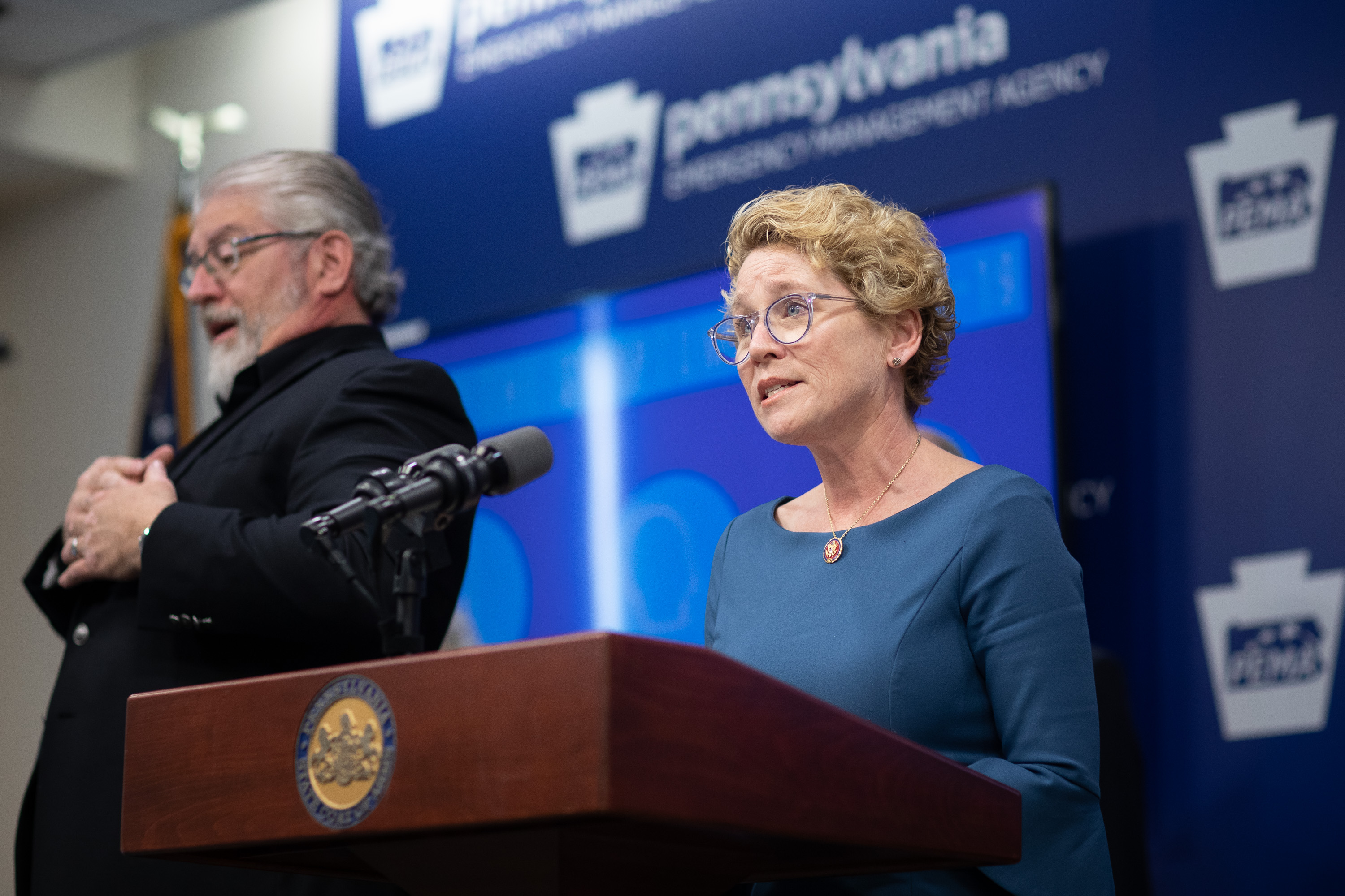 A woman in glasses speaks at a government podium during a press conference.
