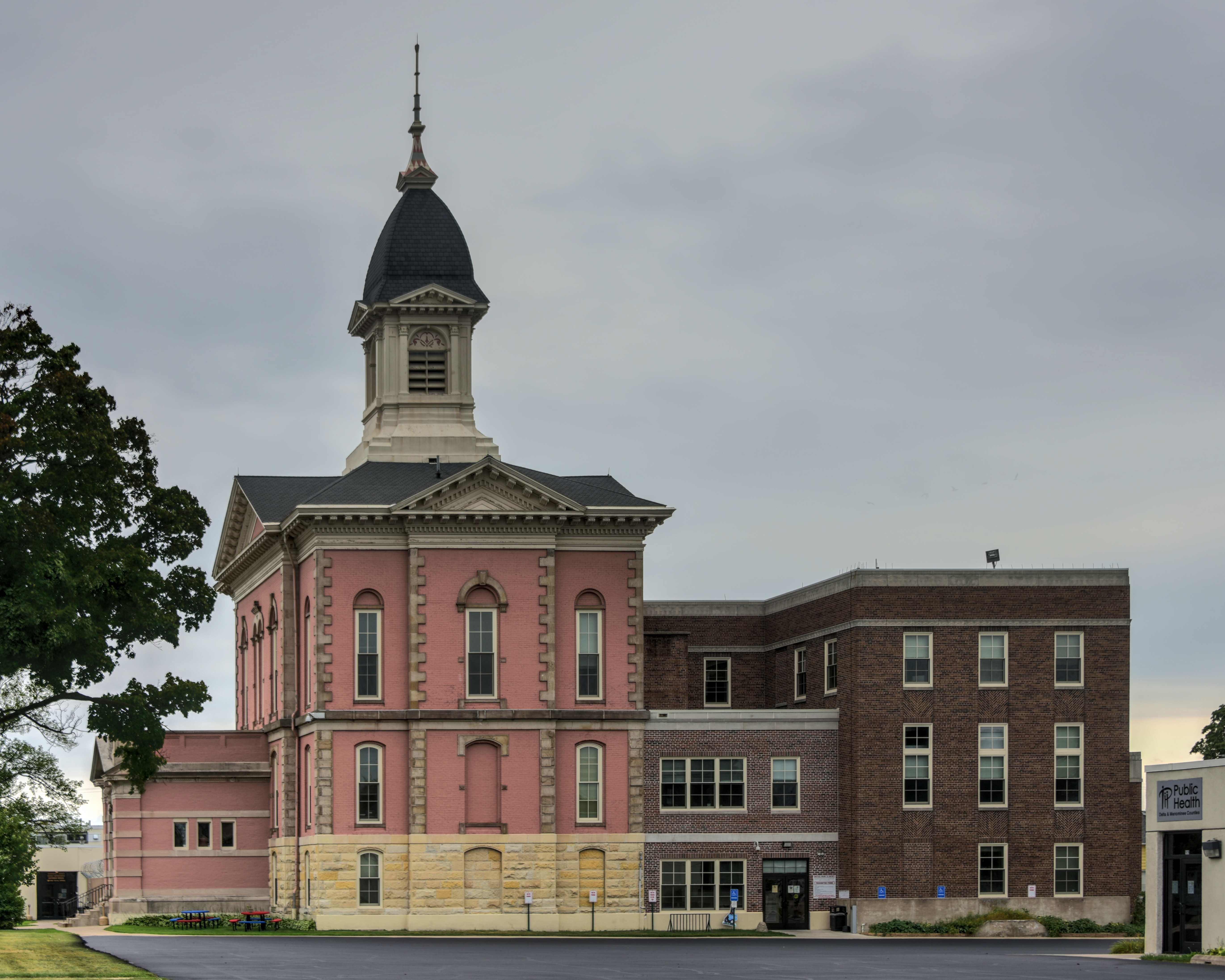 Wide view of a historic red brick courthouse with a cupola and a newer brick addition alongside it.