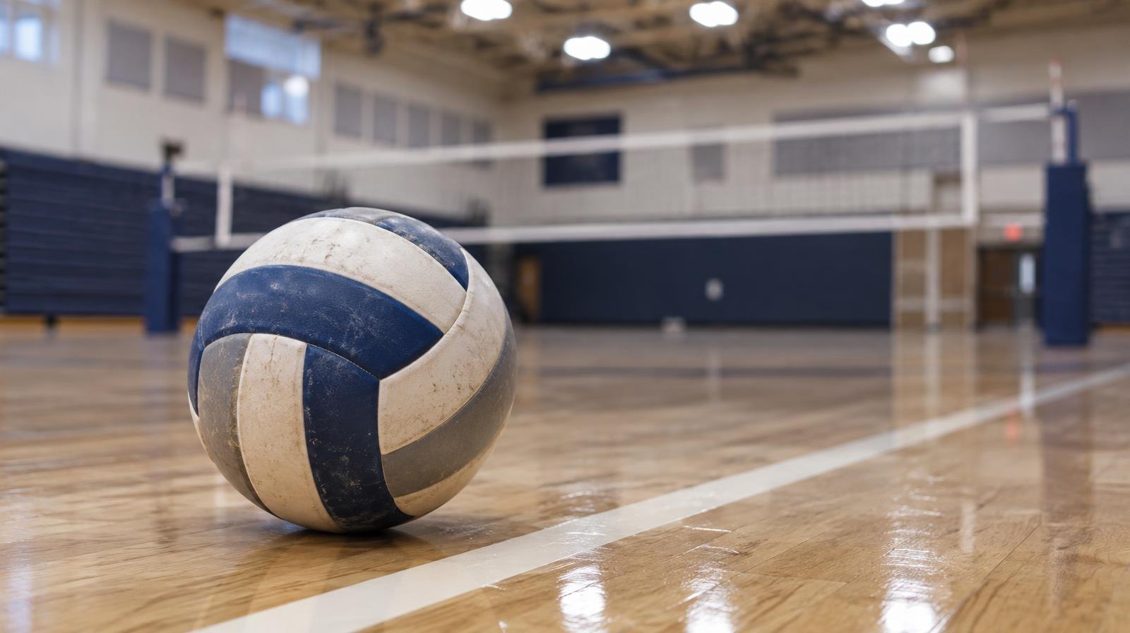 A volleyball resting on a hardwood gym floor beside a painted court line.