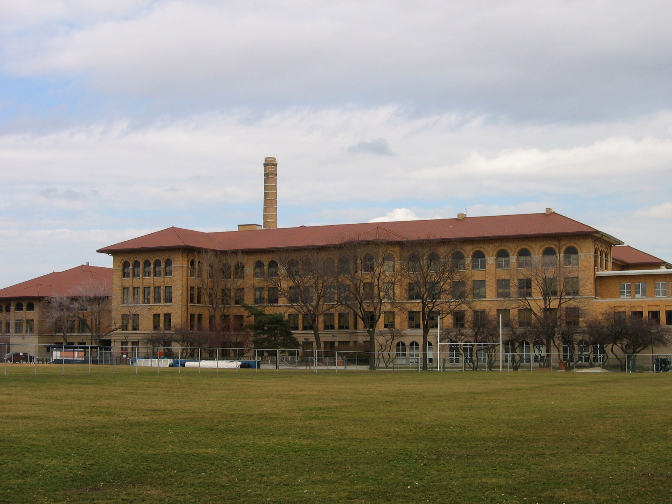 Large brick high school building with arched windows viewed from a grassy athletic field.