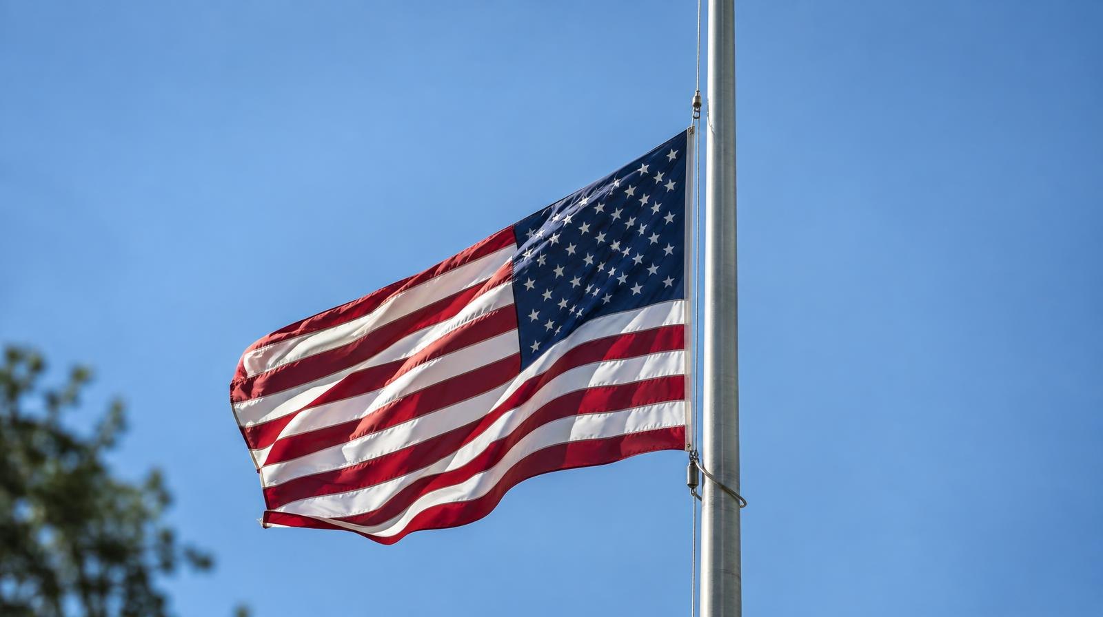 American flag lowered to half-staff on a tall metal flagpole.