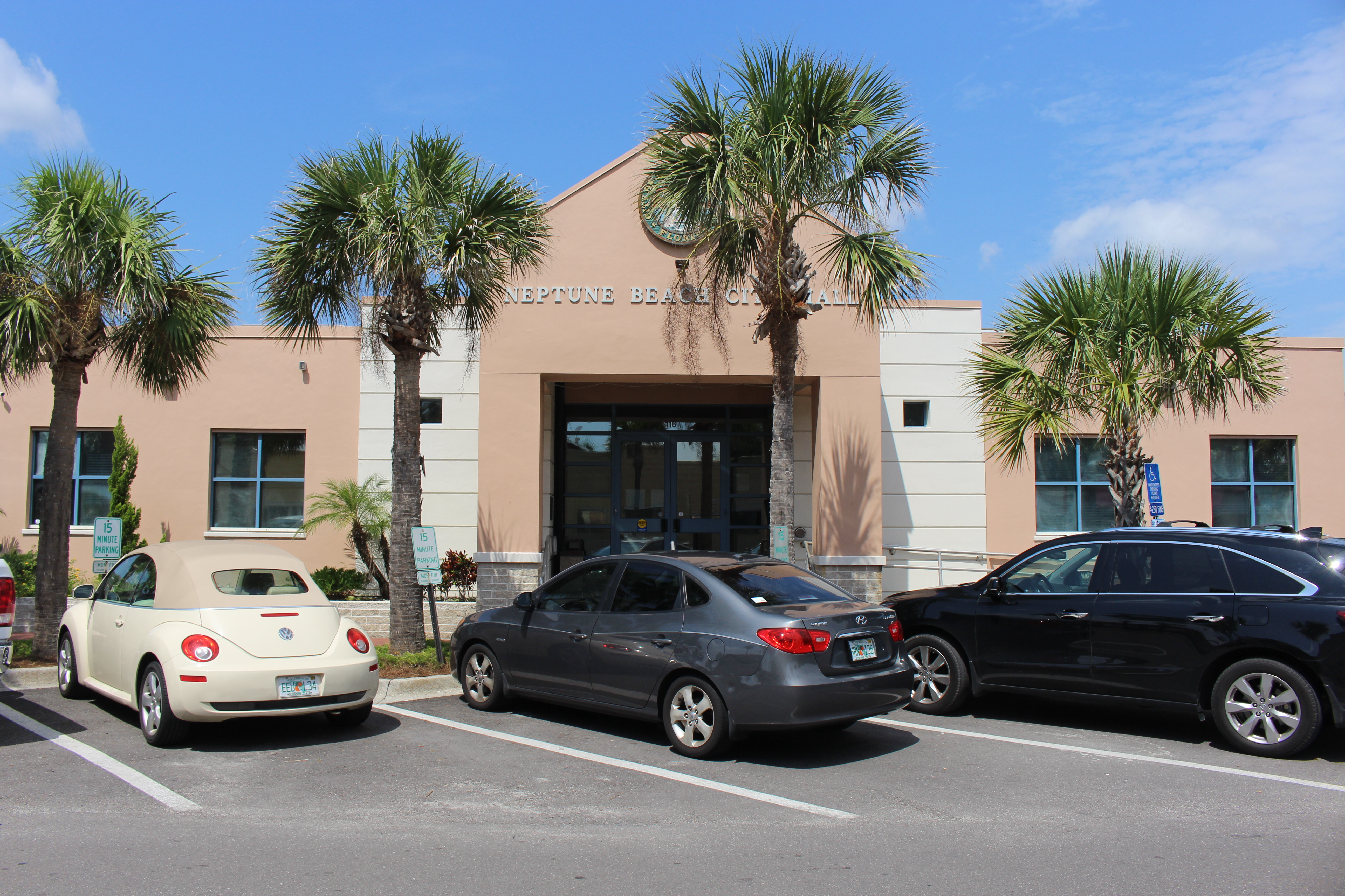 Low-rise municipal building with palm trees and cars parked in front on a sunny day.